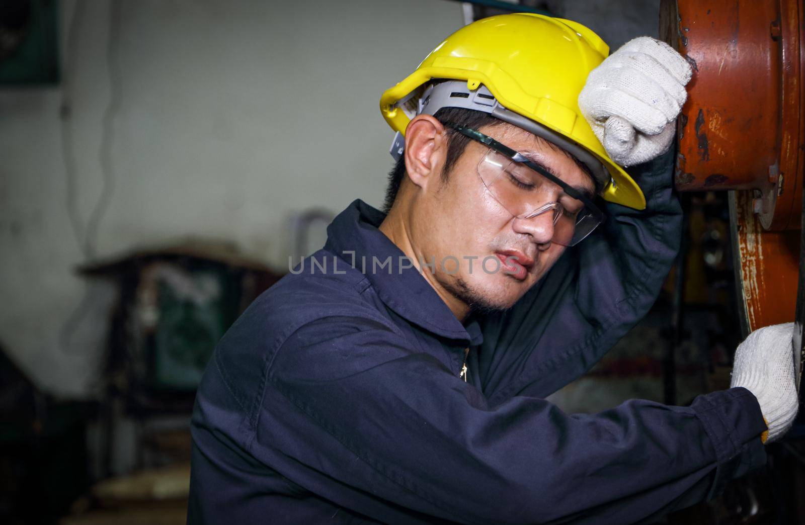 Asian male worker Dressed in uniform, helmets and safety glasses, taking a nap after work, inspection, maintenance of a metal press at the factory.