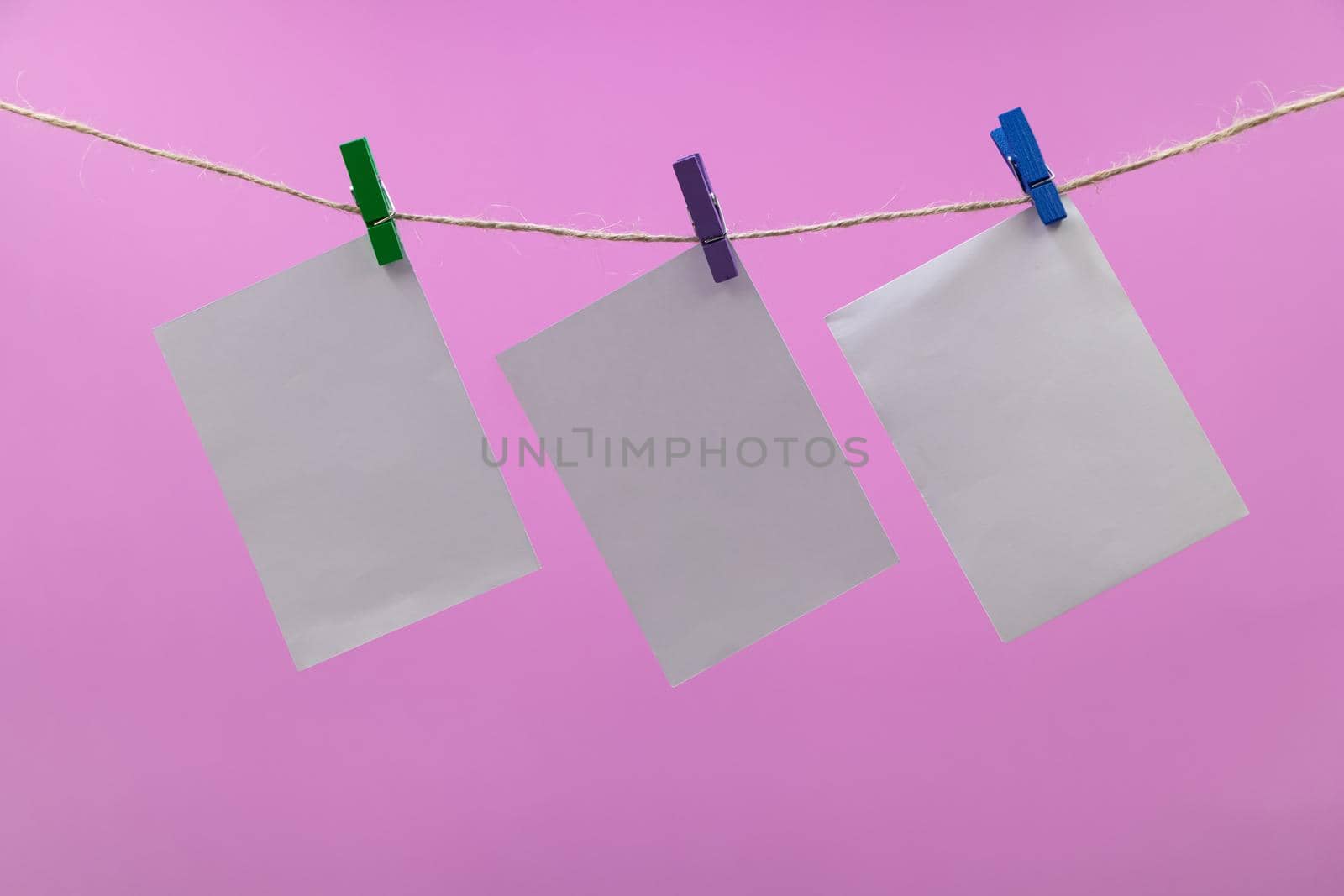 Empty paper sheets for notes, frames that hang on a rope with clothespins pink colored background, collection of various notes, Mockup template for memories, and a clothes pegs on white background. Blank cards on the rope.