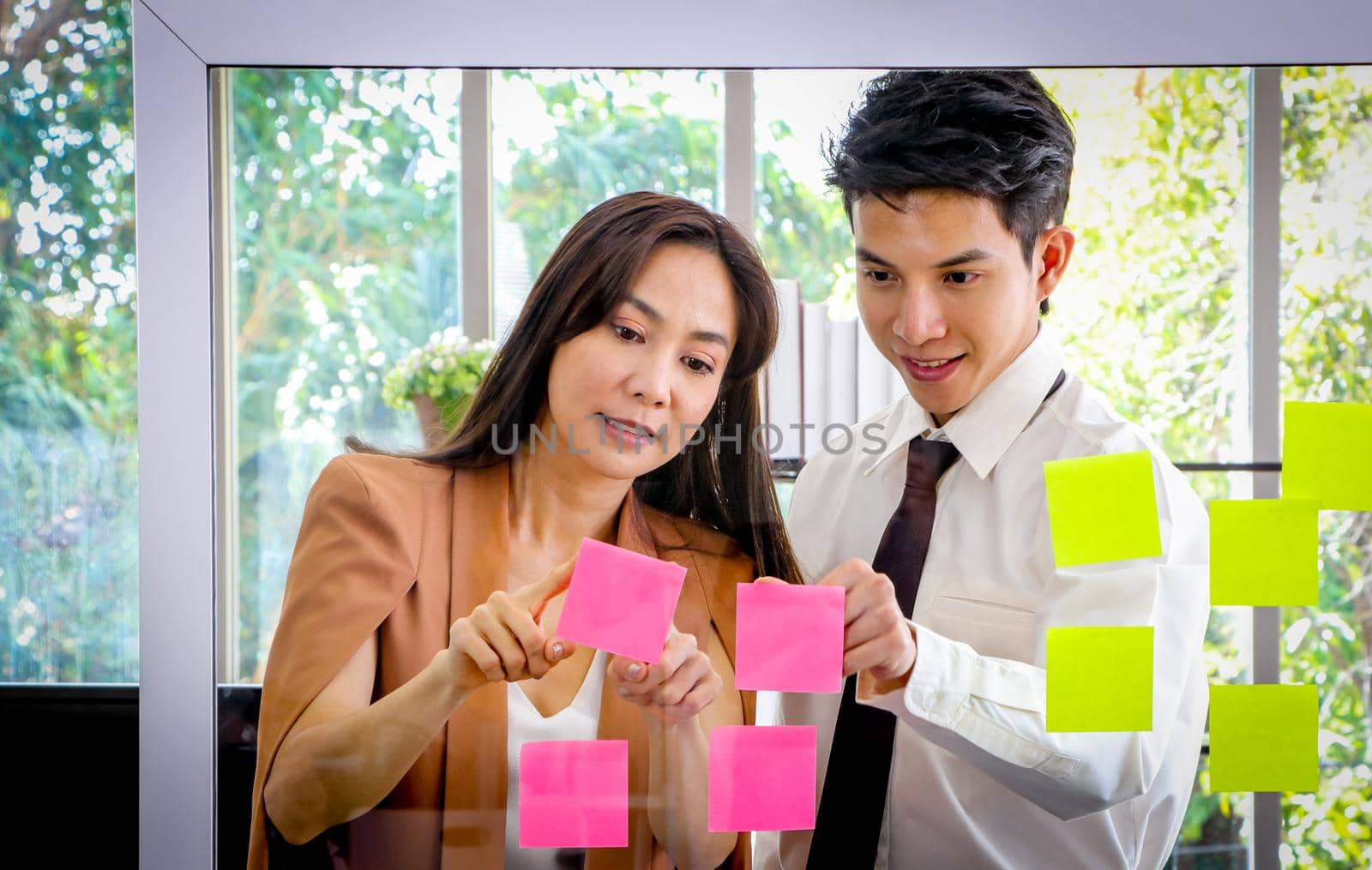 Asian businessmen and women looking and writing post-it notes for brainstorming. Put a post on the mirror in the office Work plan, brainstorm, strategy Creative Lifestyle, Success in Business Concept