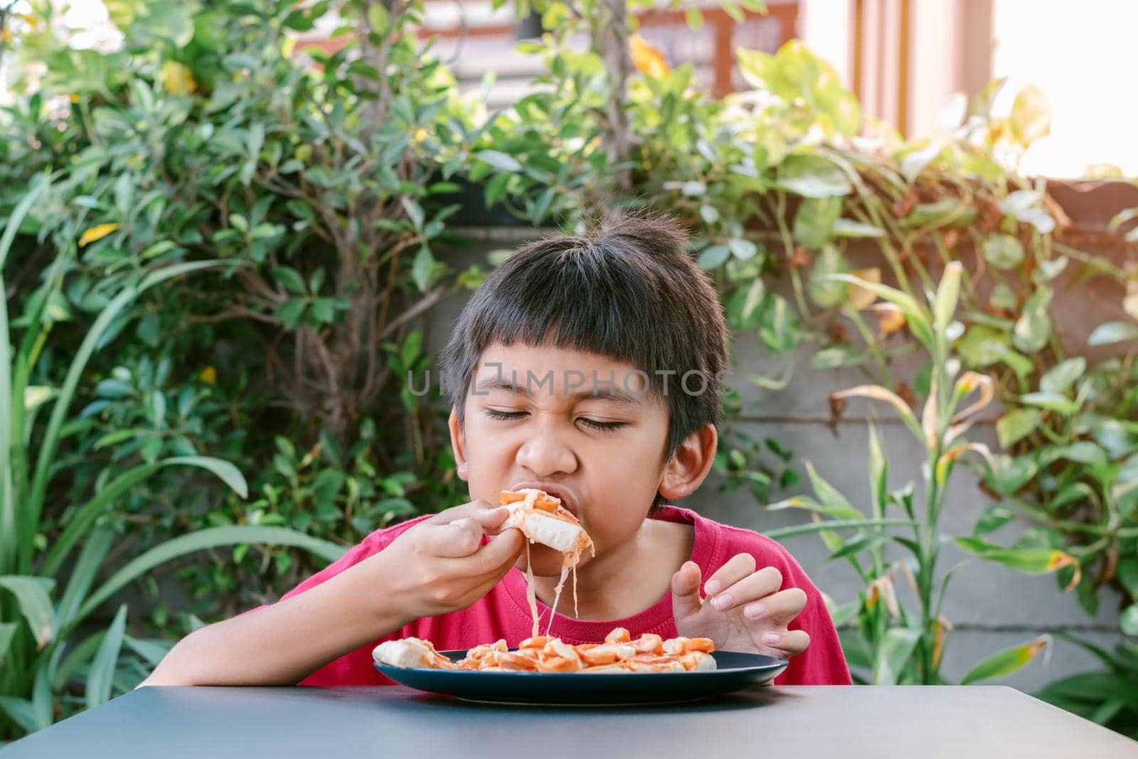 Asian cute boy in red shirt eating pizza deliciously and happily.