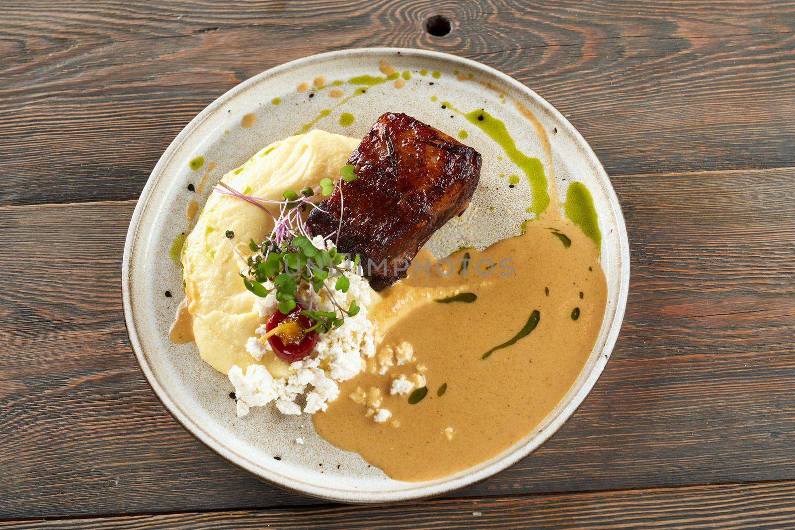 From above view of juicy grilled beef steak served with mashed potato puree, cottage cheese, sauce and sprouts. Tasty dish presented on wooden table in restaurant. Cuisine concept.