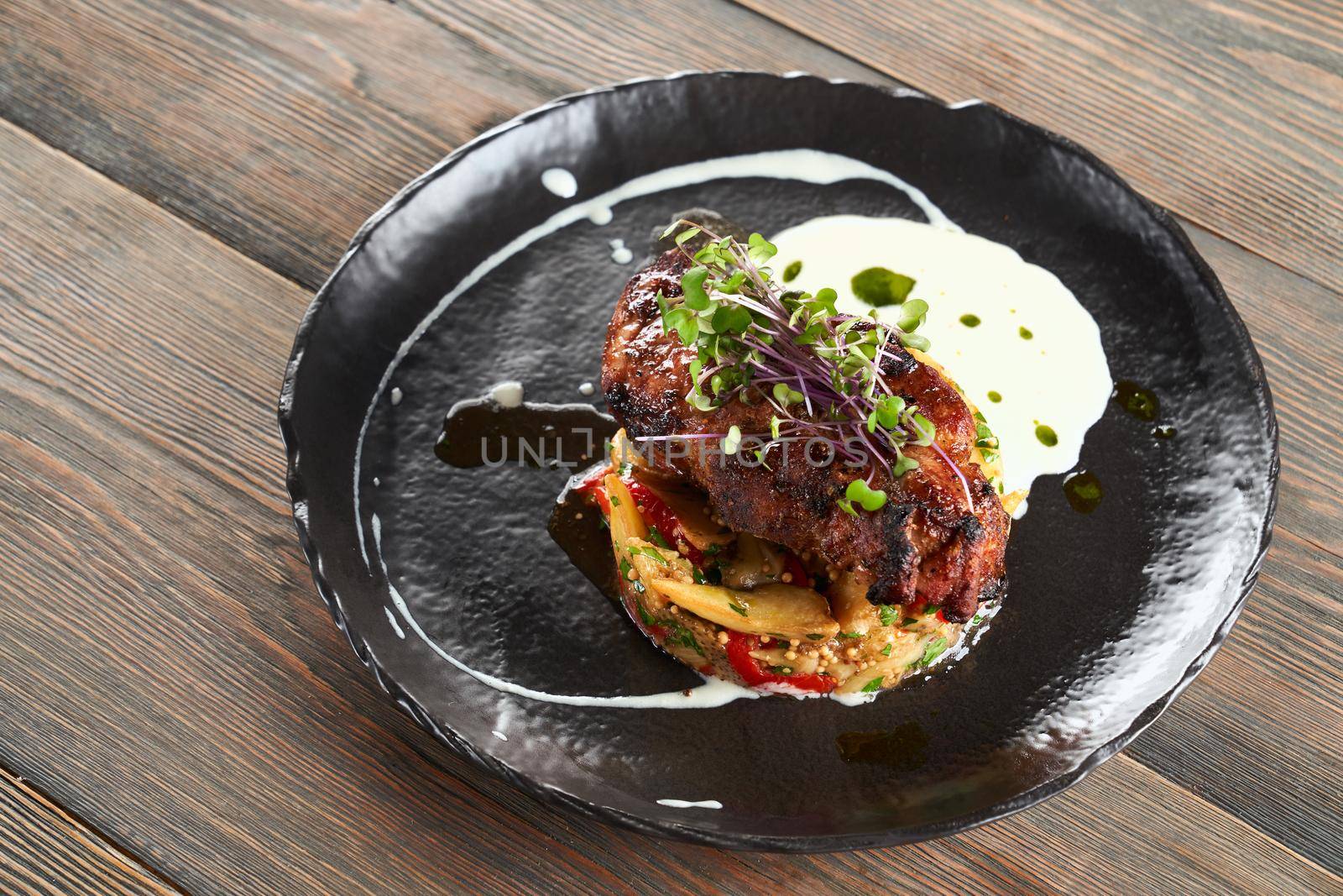 From above view of juicy grilled beef steak served on roasted vegetables pillow, sour cream and sprouts. Tasty dish in black ceramic plate presented on wooden table in restaurant. Cuisine concept.