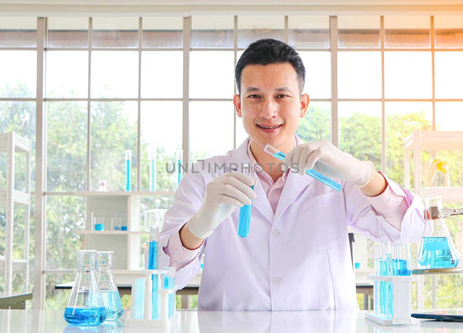 An Asian scientist or chemist drops a blue liquid chemical in a laboratory. Research concepts in healthcare, pharmacy, and medicine. Liquid analysis to separate DNA and molecules in vitro.