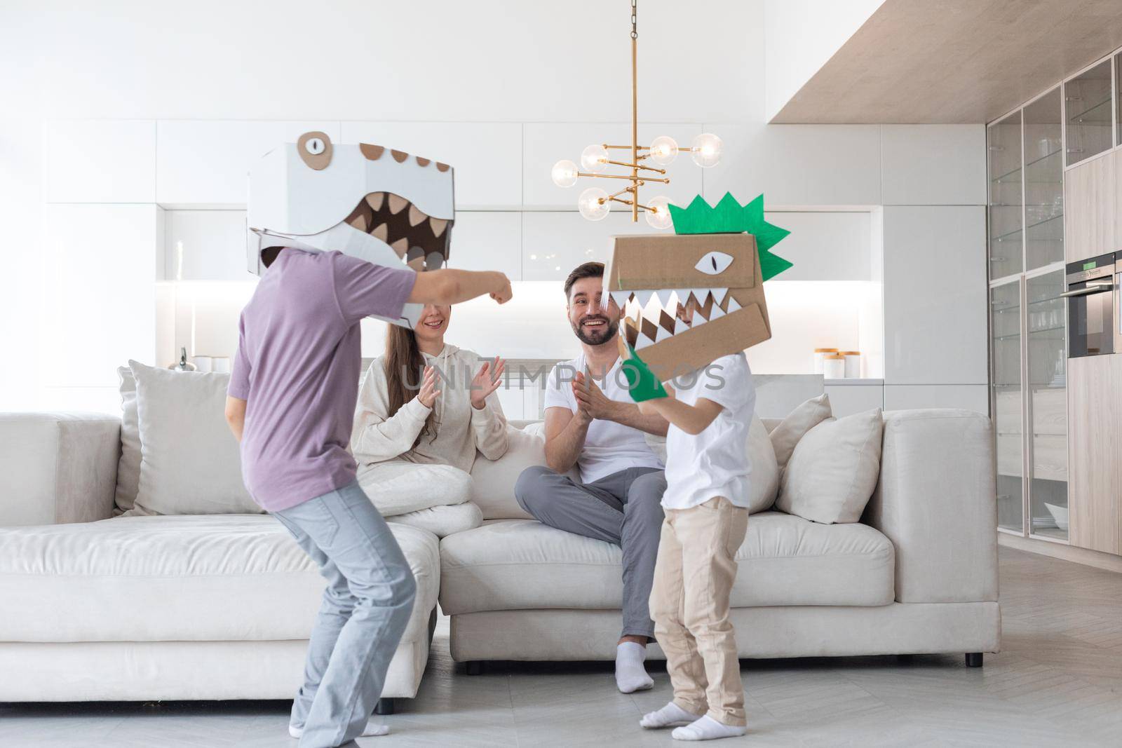 Happy family of parents and two children playing dinosaurs at home, children wearing handmade costume mask of cardboard