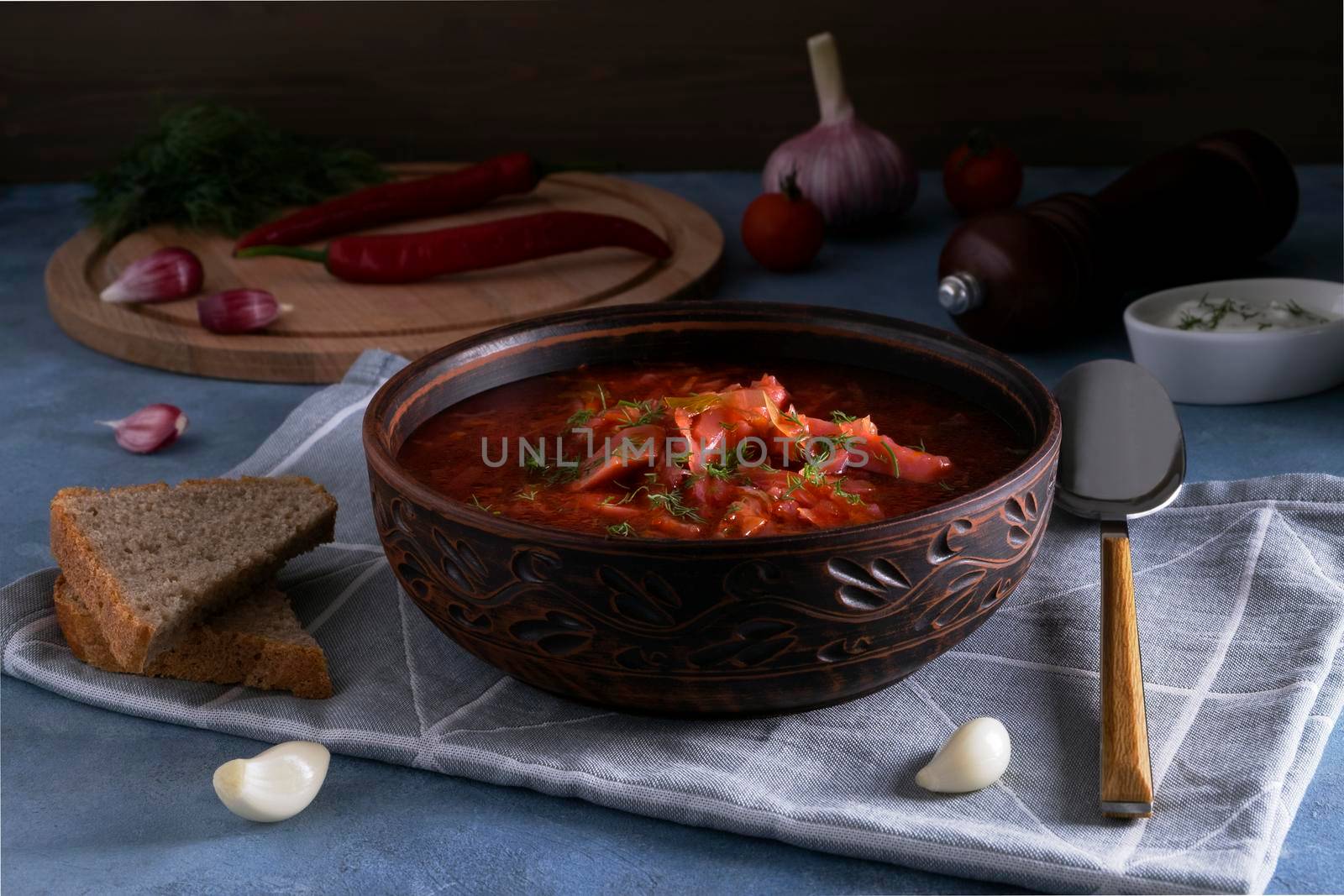 Close-up of the traditional Russian soup borscht made from cabbage, beets and other vegetables served in a clay ceramic plate with sour cream and garlic. National cuisine concept. Selective focus.