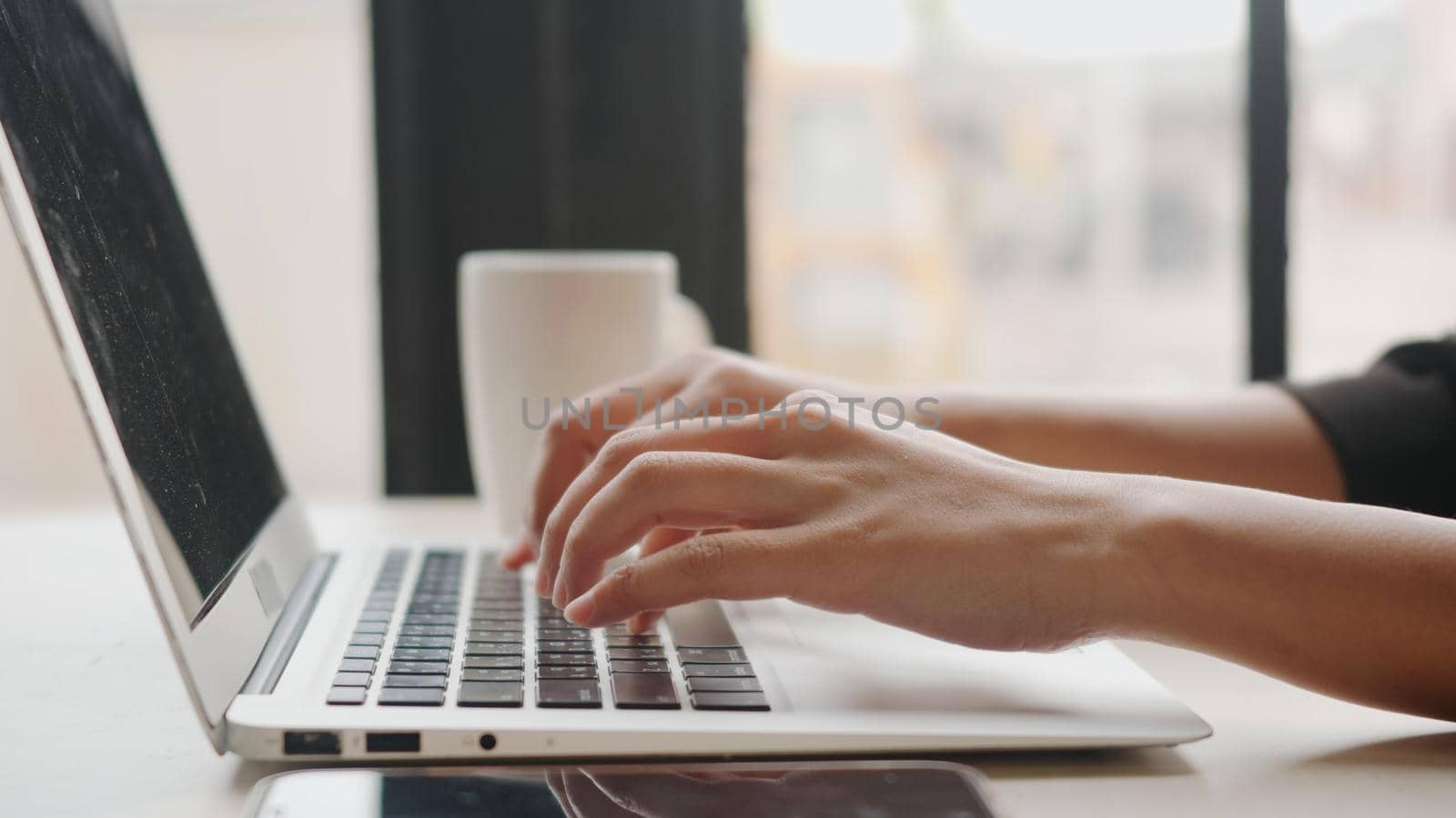 Closeup businesswoman working typing on laptop computer keyboard, young woman freelancer busy while using notebook, female workspace at coffee cafe shop