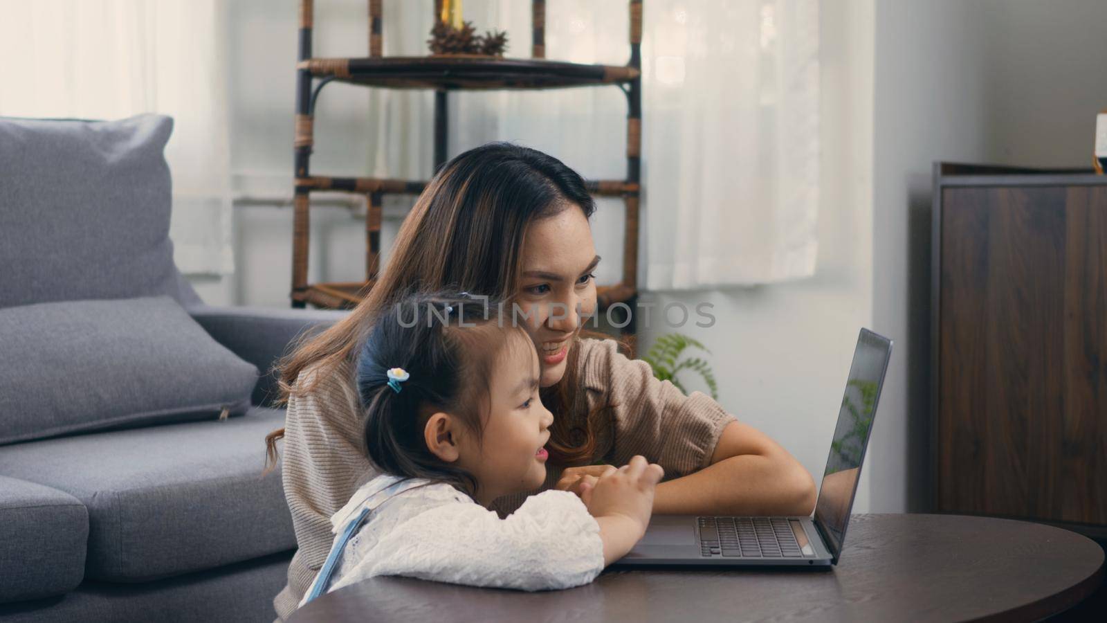 mother with laptop computer teaching her kid to learn or study online by Sorapop