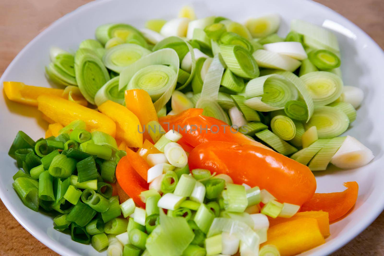 Sliced leeks, peppers and spring onions in a white bowl