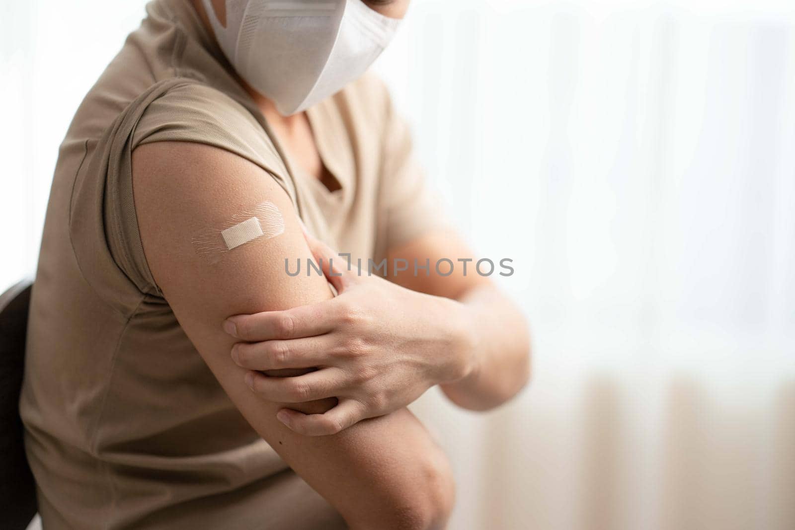 Man wearing mask arm with bandage showing his arm after receiving vaccine.