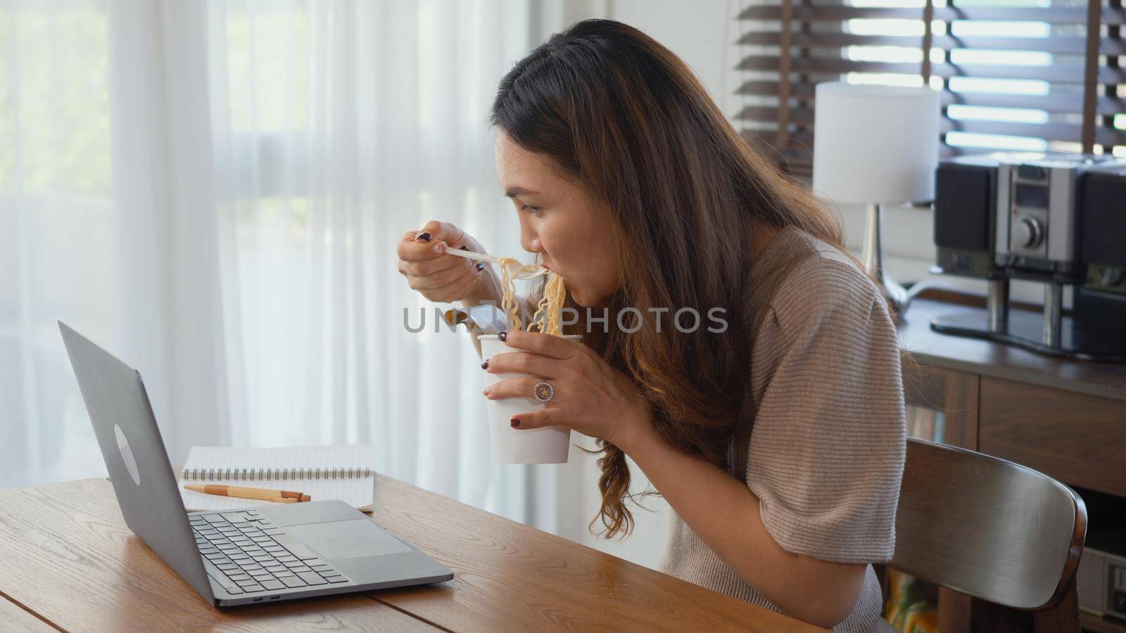business woman eating instant noodles while working on laptop computer by Sorapop