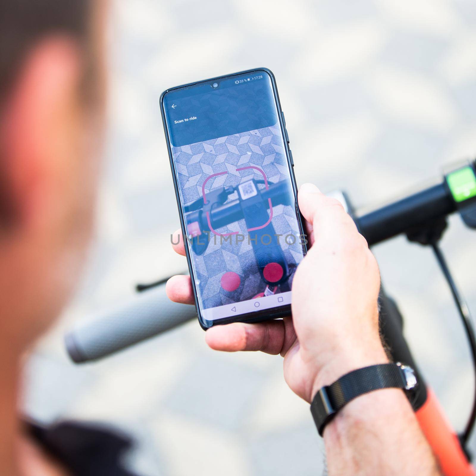 Close up of hand and smartphone, unlocking dockless electric scooter for rent with debranded generic phone app. by kasto