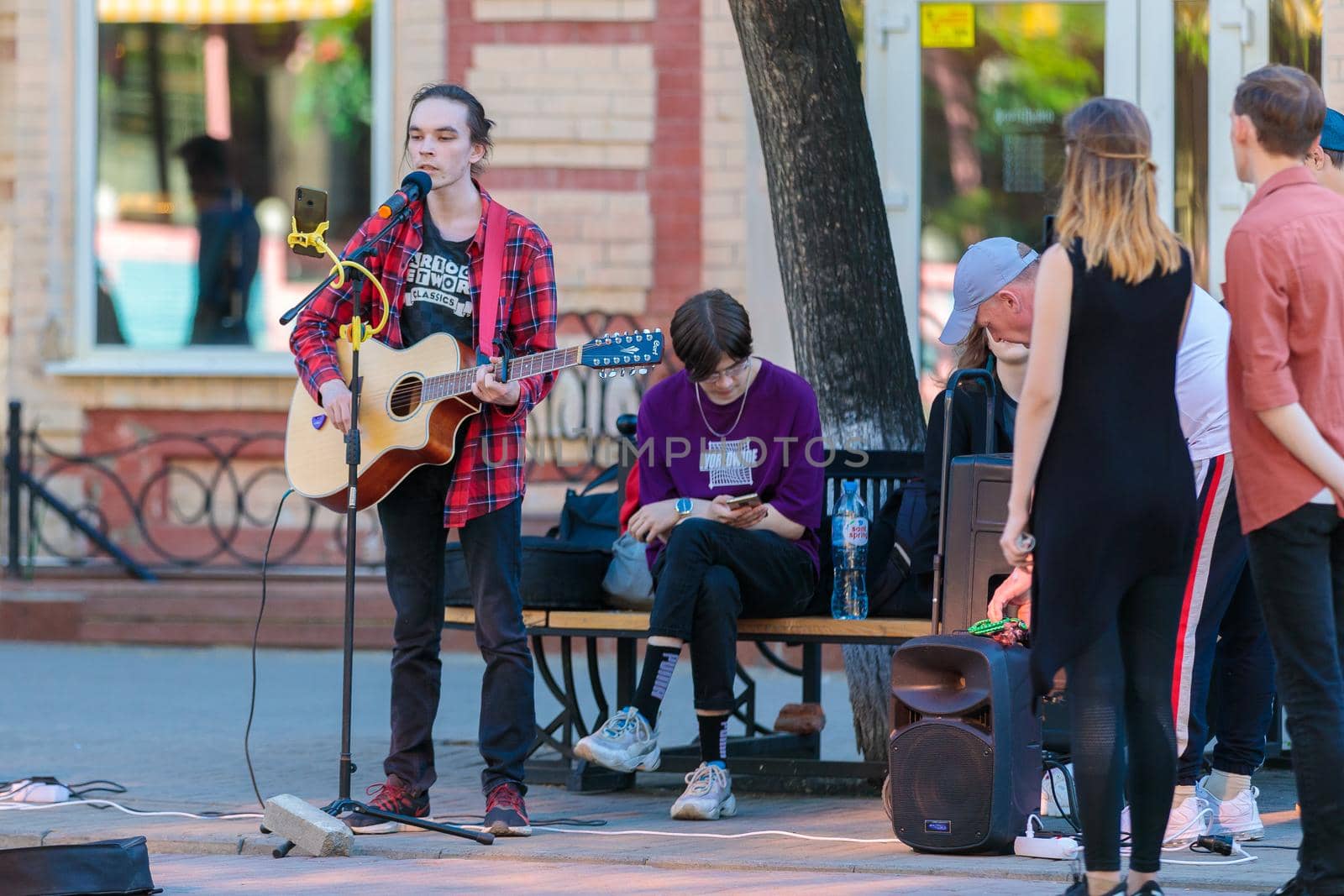 A young guy stands with a guitar on a central street, plays and sings, earning money. Chelyabinsk, Russia, May 17, 2021