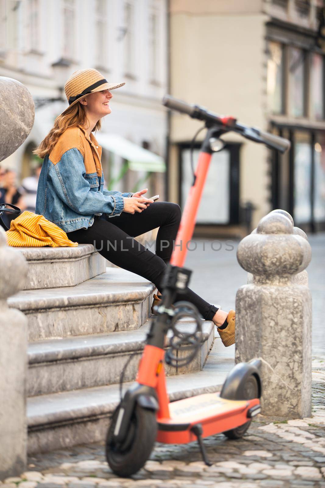 Traveler exploring Ljubljana's old medieval historical city on environmentally friendly electric scooter. Female tourist exploring old city center, sitting and resting on fountains' stairs