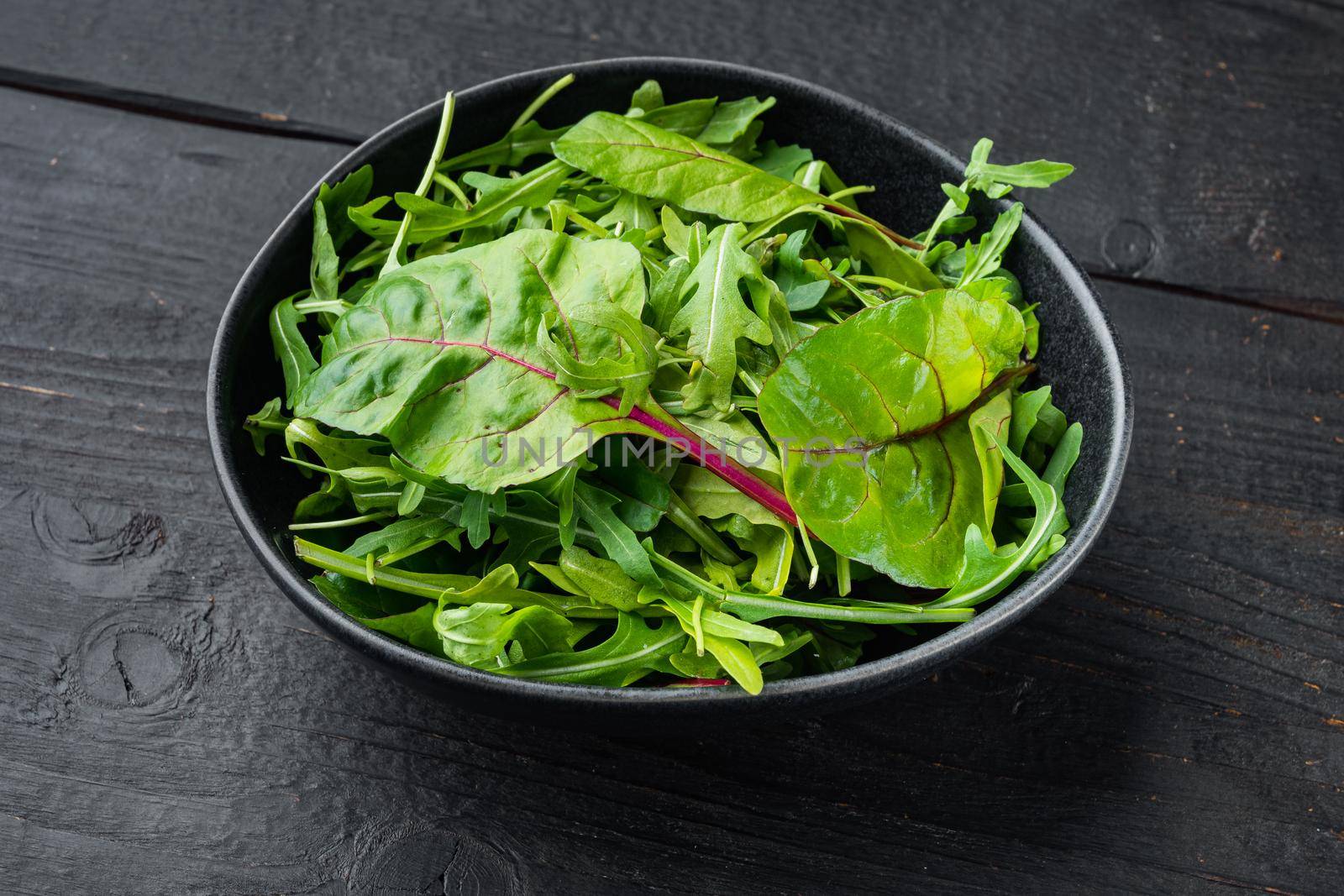 Arugula, Chard herbs mix , on black wooden table background by Ilianesolenyi
