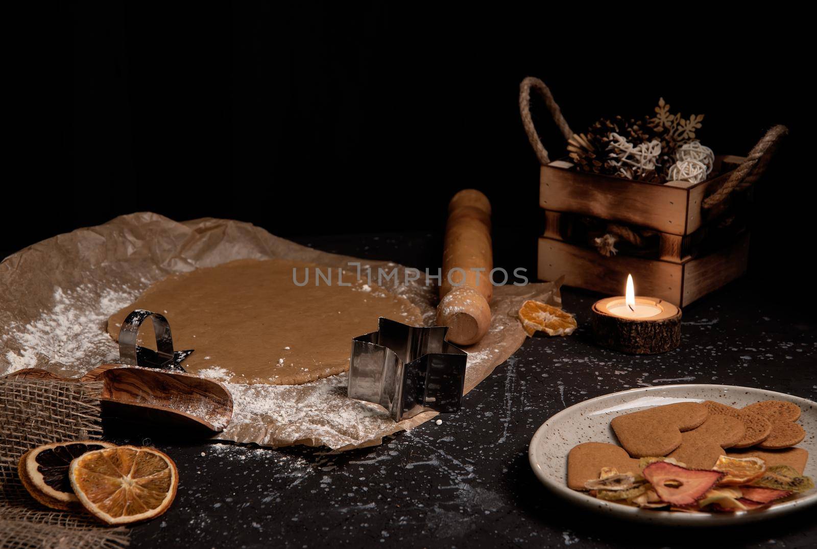 Christmas and new year celebration cooking table with prepairing gingerbread cookies dow, decor, candle, dry oranges, stars shape tool