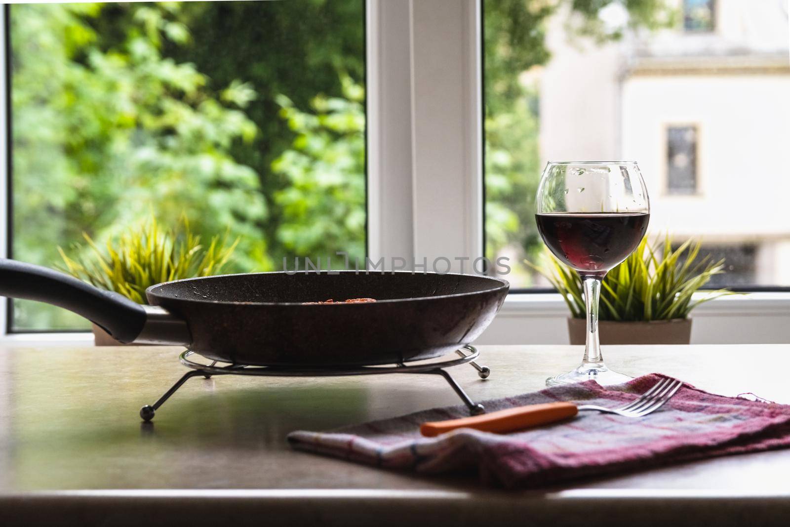 Teflon frying pan and glass of wine on a table against the window by Estival