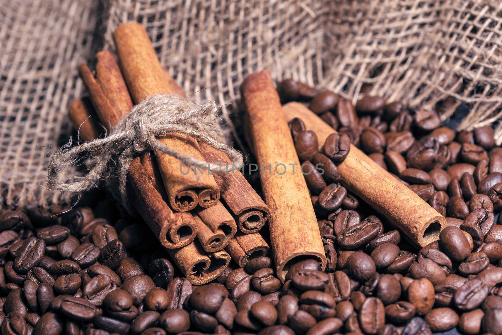 Coffee beans and cinnamon sticks lying on a table with a rough bag