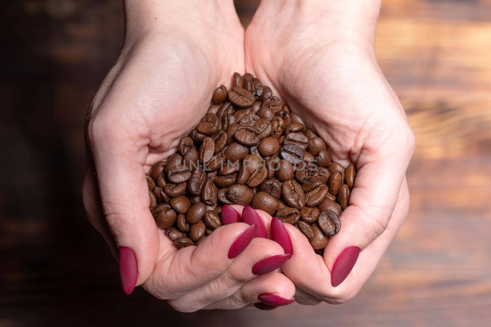 Fresh roasted coffee beans pouring out of cupped woman hands on a wooden background