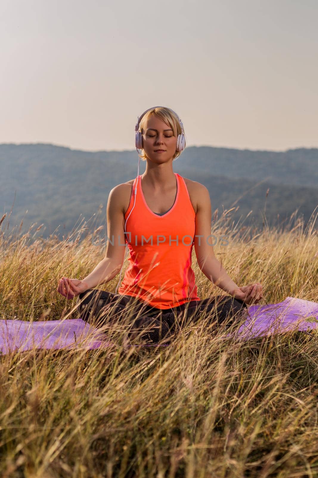 Beautiful woman sitting in lotus position with headphones and meditating in the nature. by Bazdar