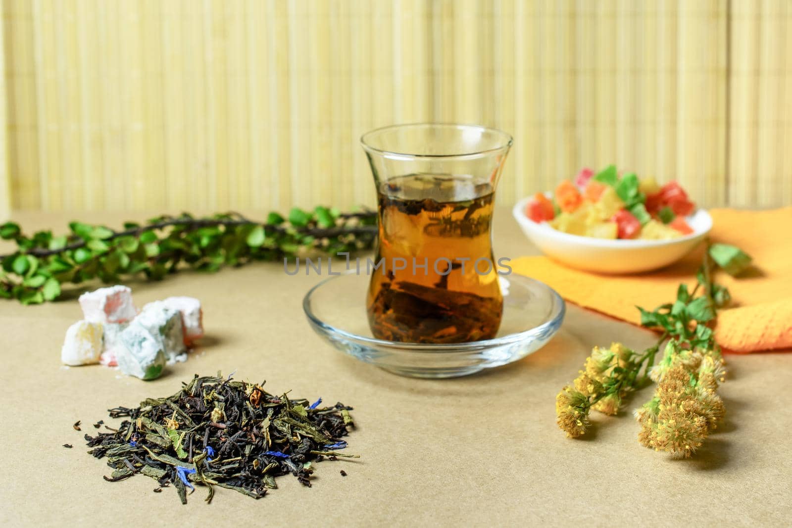 The Turkish traditional glass with tea on a table, nearby a small group of the filled dry tea, the Turkish sweets and a grass