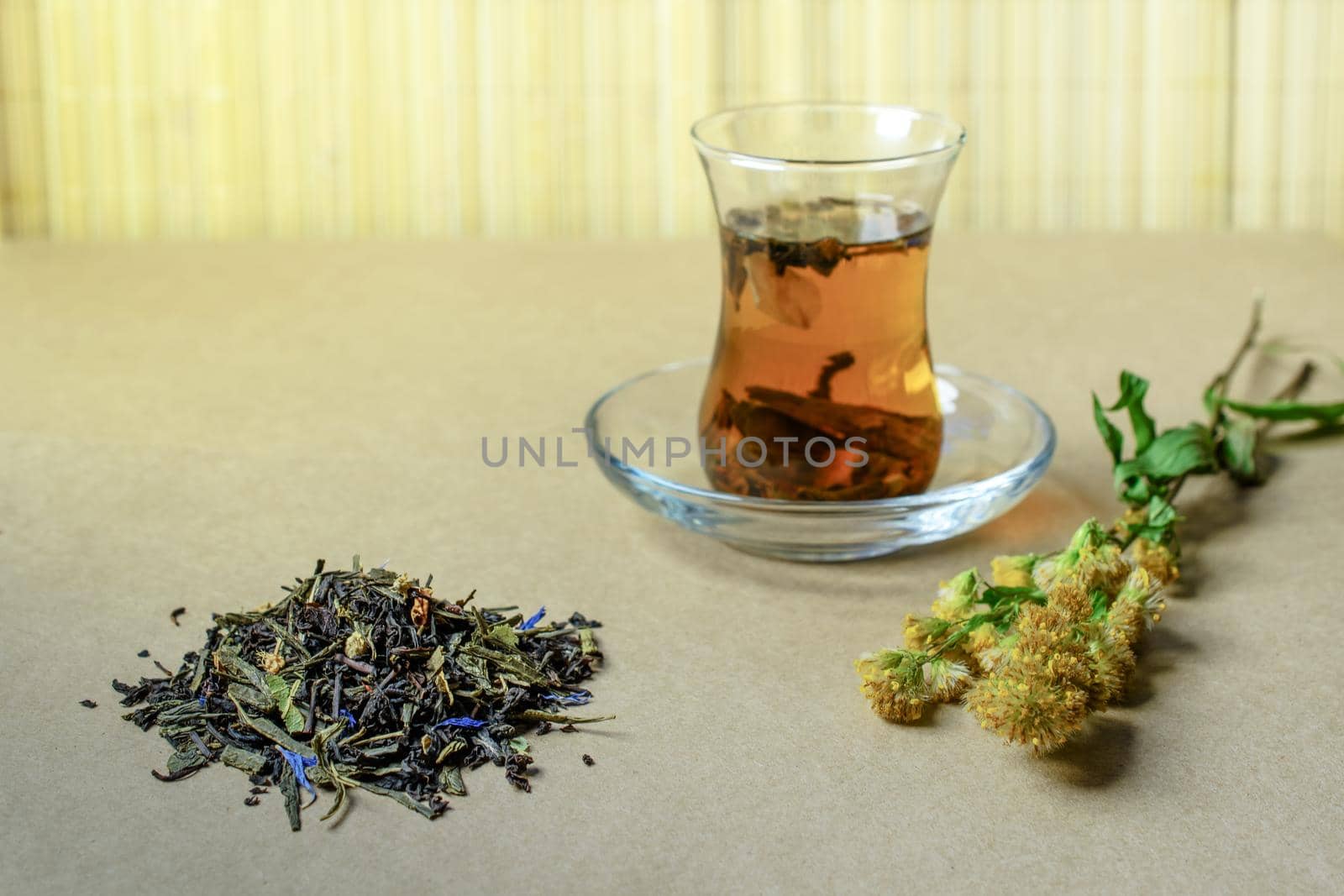 The Turkish traditional glass with tea on a table, nearby a small group of the filled dry tea and a grass by Estival