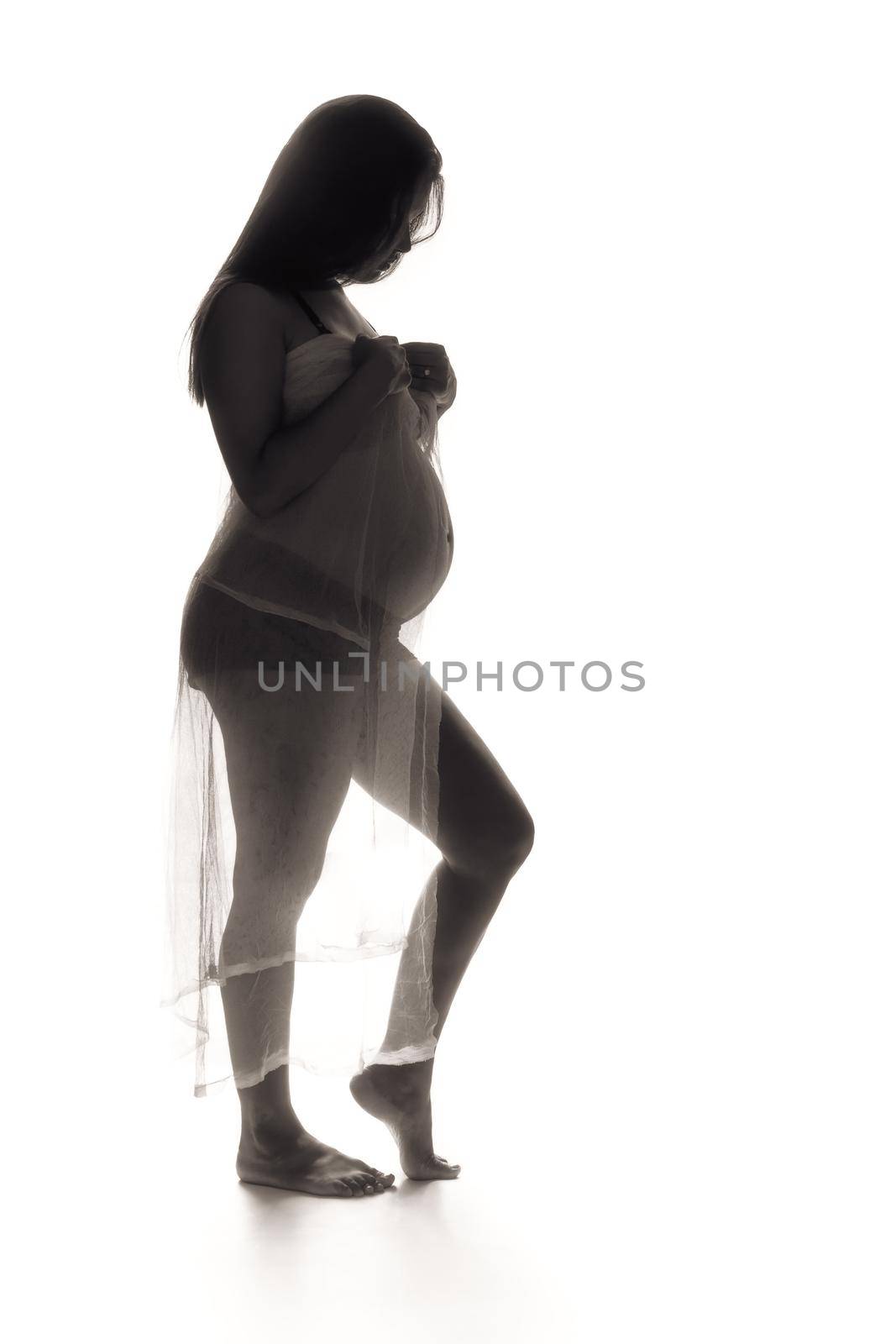 Backlit low key photo of a young pregnant woman.