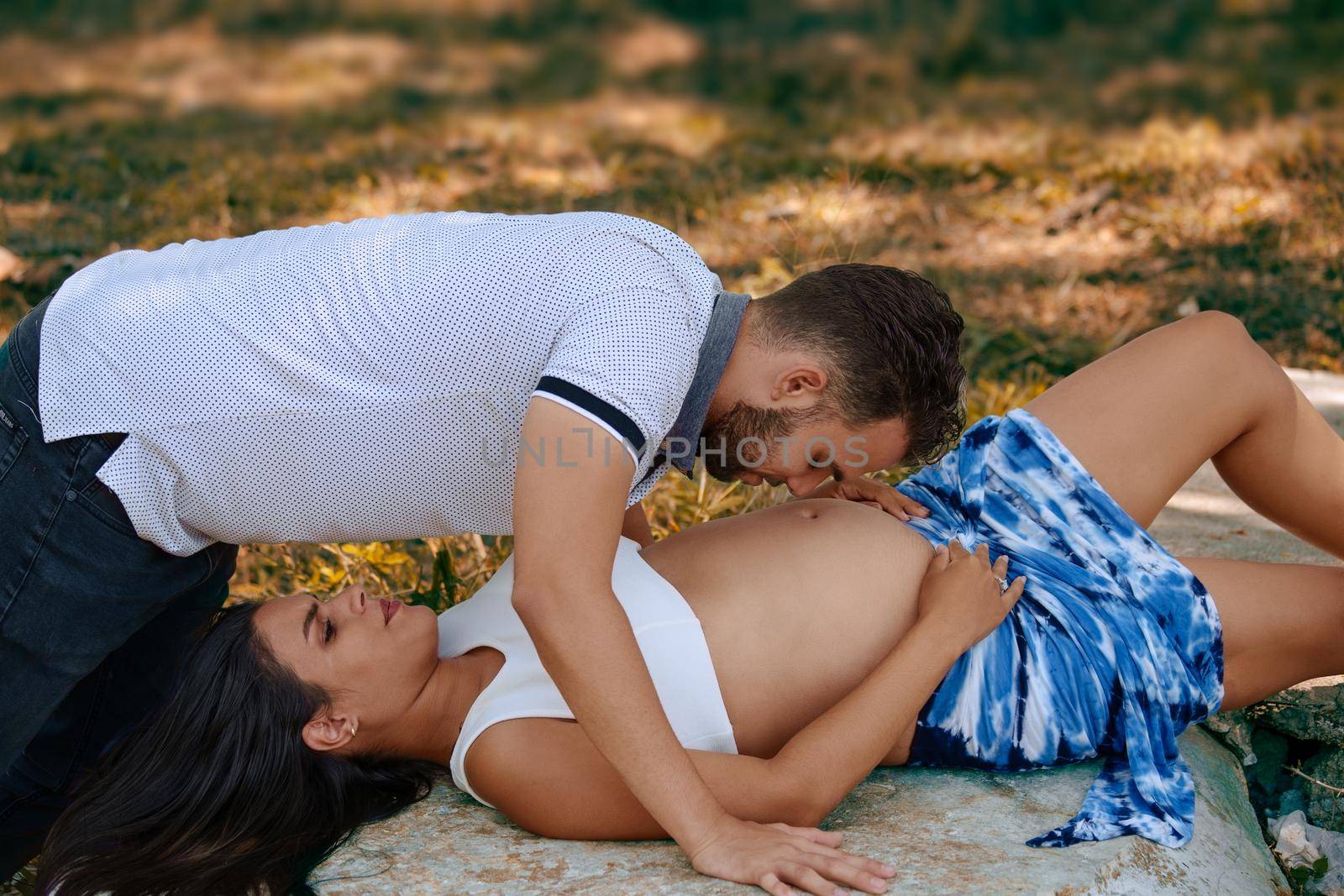 Photo of a young pregnant woman lying on her back on a rock and a young man on her