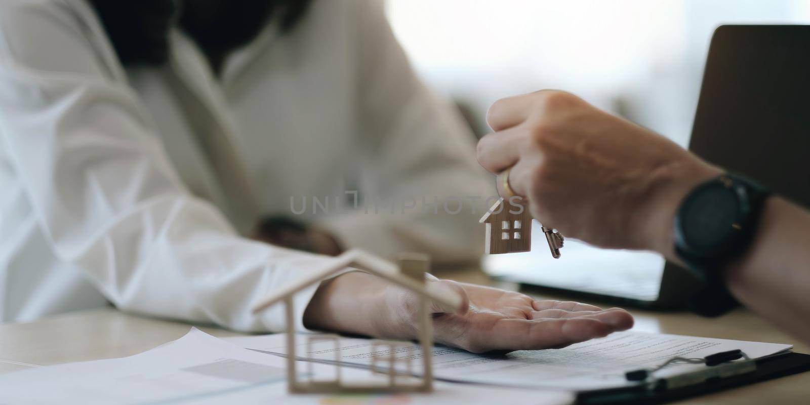real estate agent holding house key to his client after signing contract agreement in office,concept for real estate, moving home or renting property by wichayada