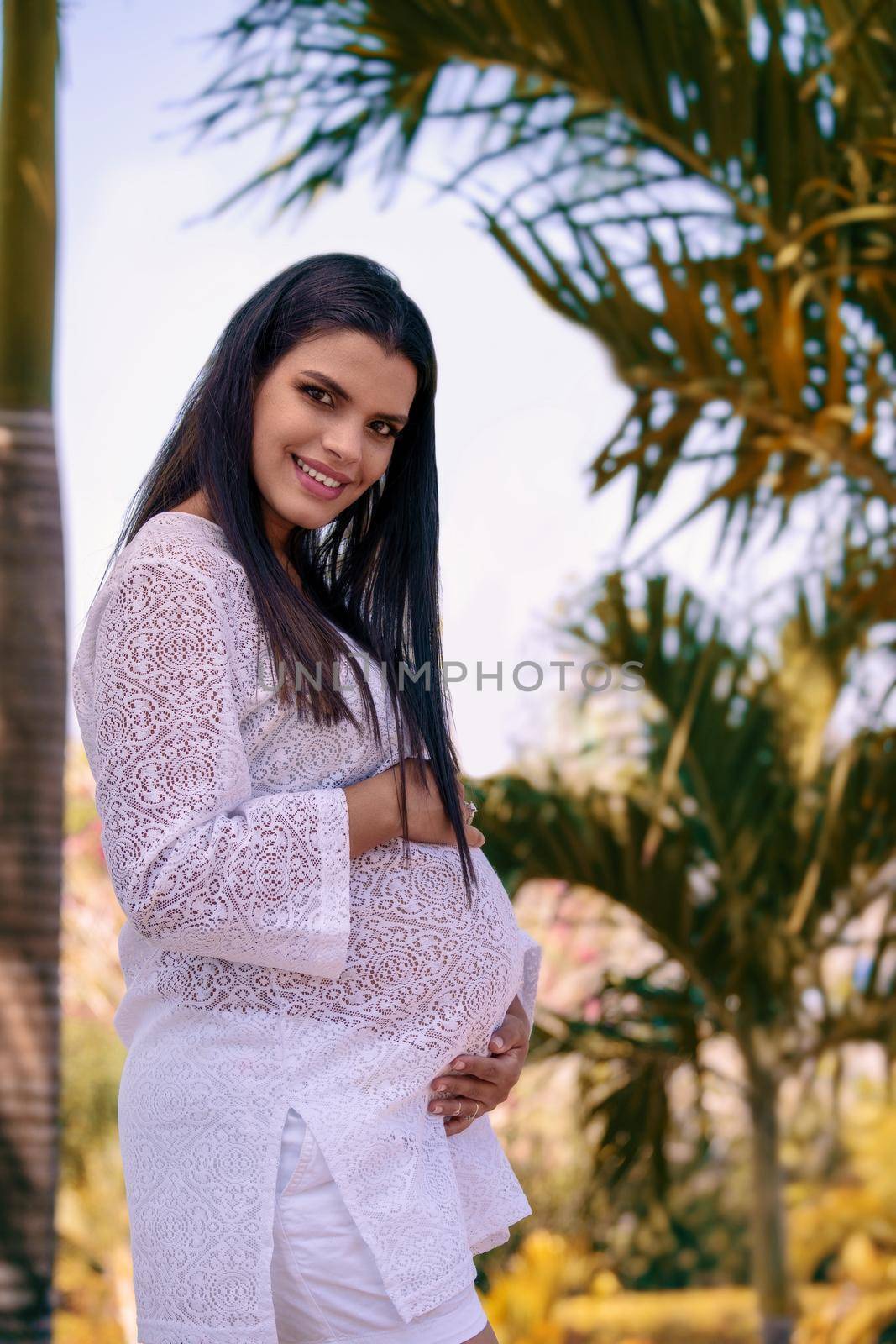 Outdoor photo of a pregnant young woman wearing white clothes