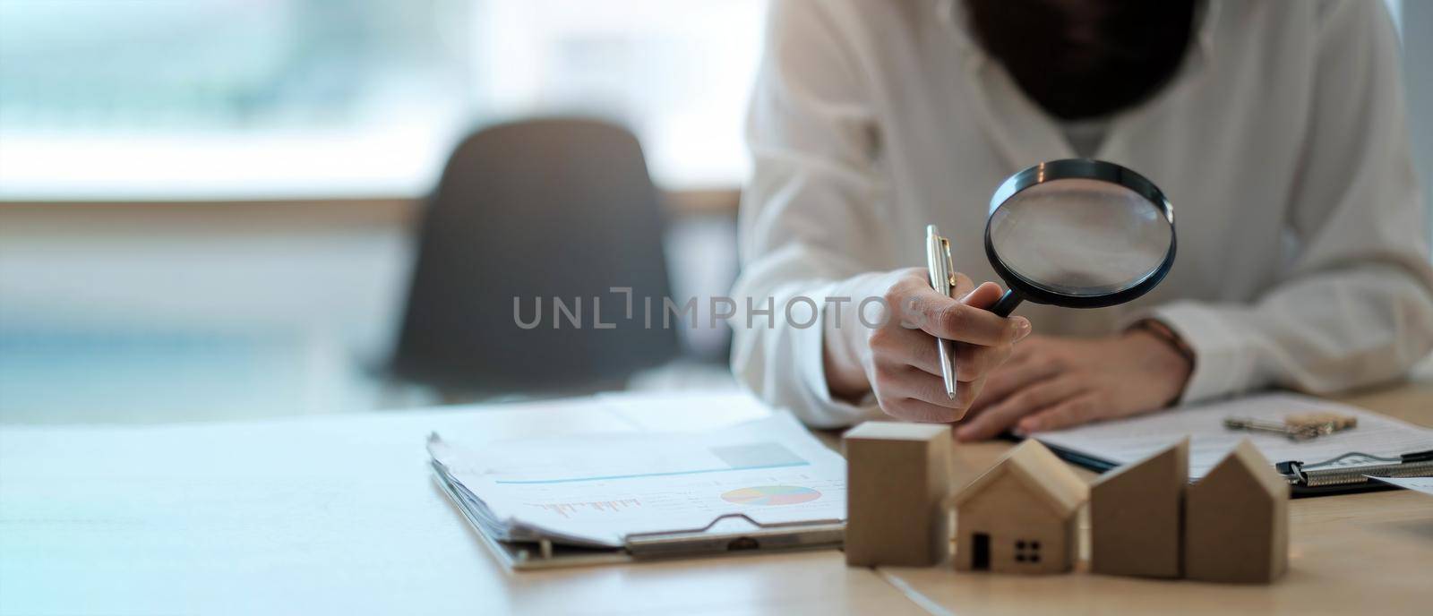 a woman looks at the house with a magnifying glass and on the table paper and data..