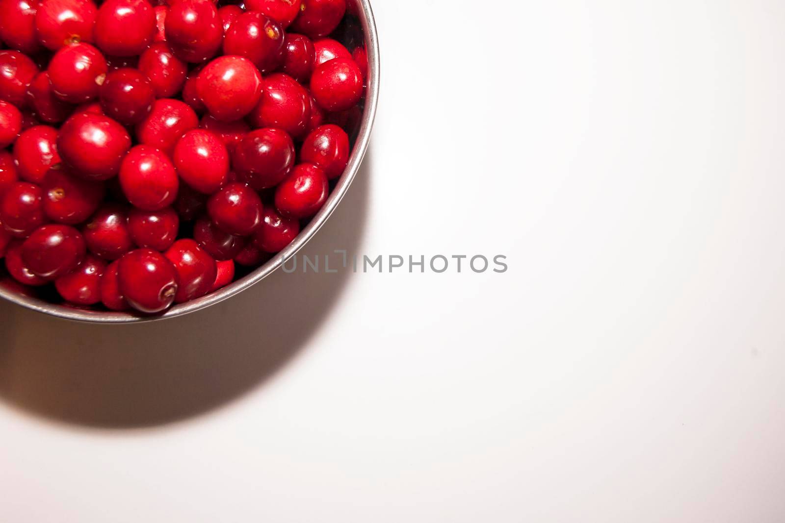 Bowl of cherries on a white background. Red cherries. Bowl placed on the top left corner of the frame