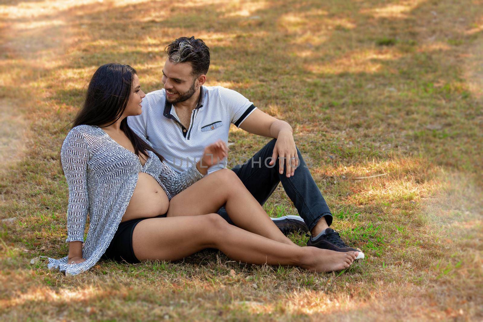 Young couple sitting on the grass. The young woman is pregnant