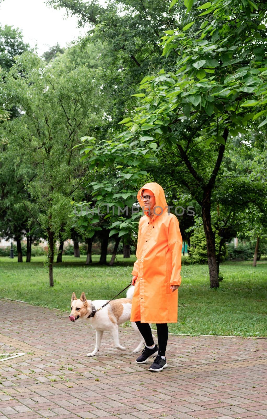 young woman in orange raincoat walking with her dog in a park by Desperada
