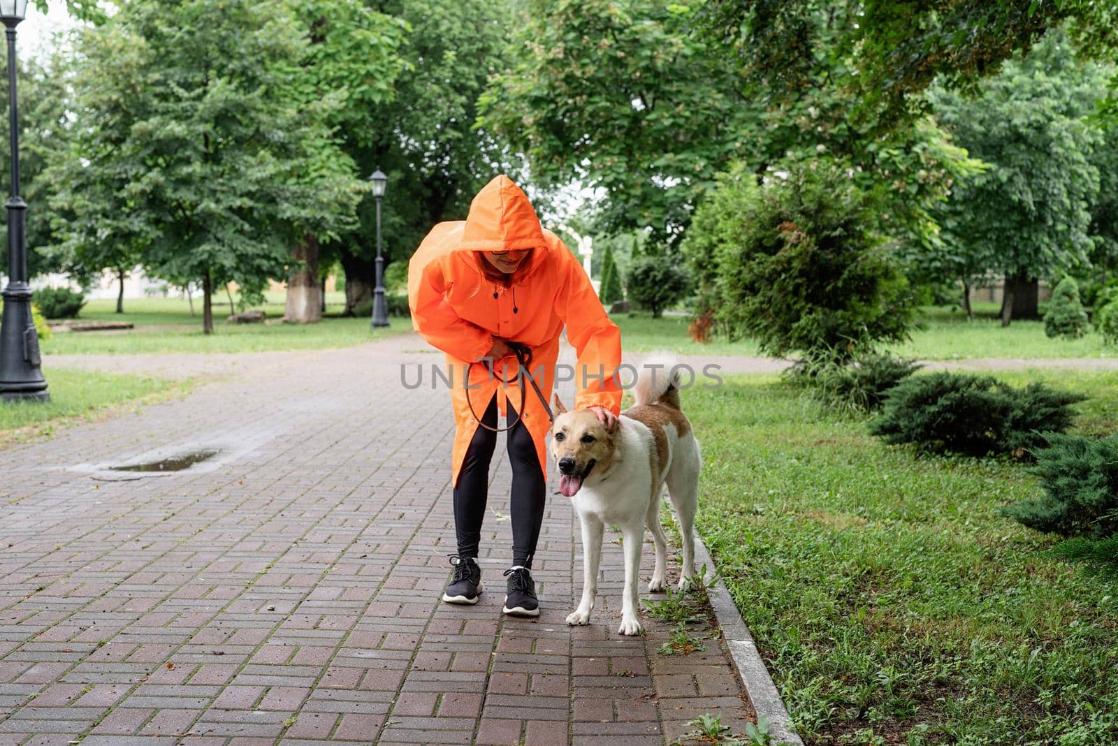 young woman in orange raincoat walking with her dog in a park by Desperada