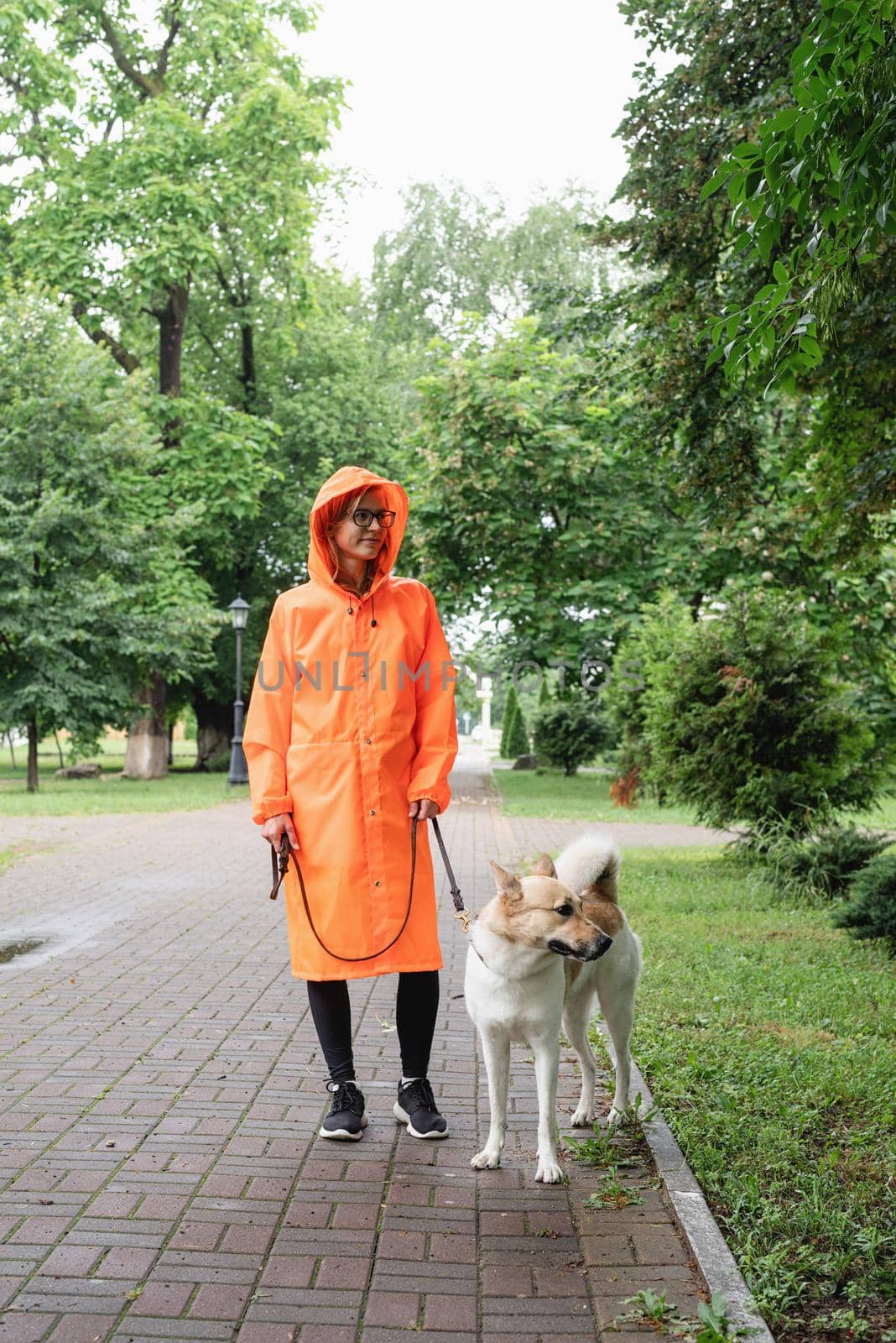 young woman in orange raincoat walking with her dog in a park by Desperada