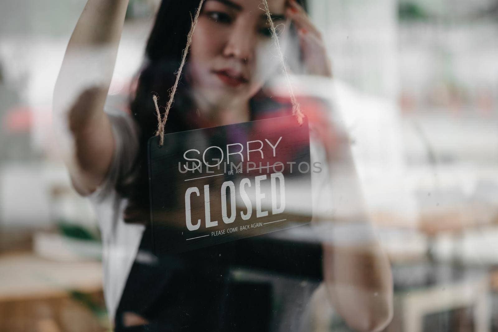 Close up shot of woman entrepreneur hand turning close sign board on glass door in coffee shop or restaurant during coronavirus lockdown quarantine.Owner small business, food and drink, business reopen again concept.