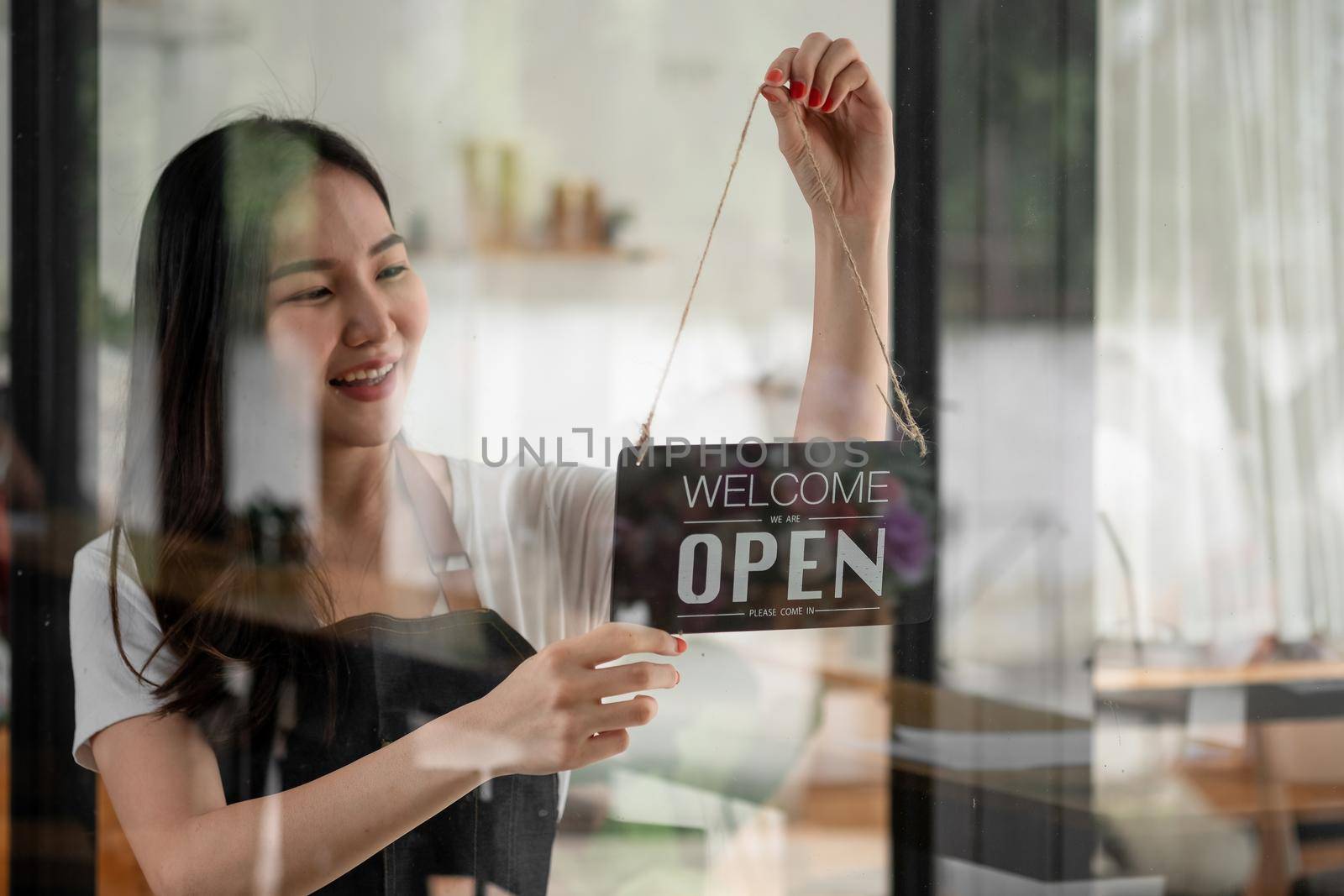 Portrait of smiling young barista girl in apron holding open sign board while standing at her cafe. elegant asian coffee shop female staff turn door plate in the morning in own store small business by nateemee