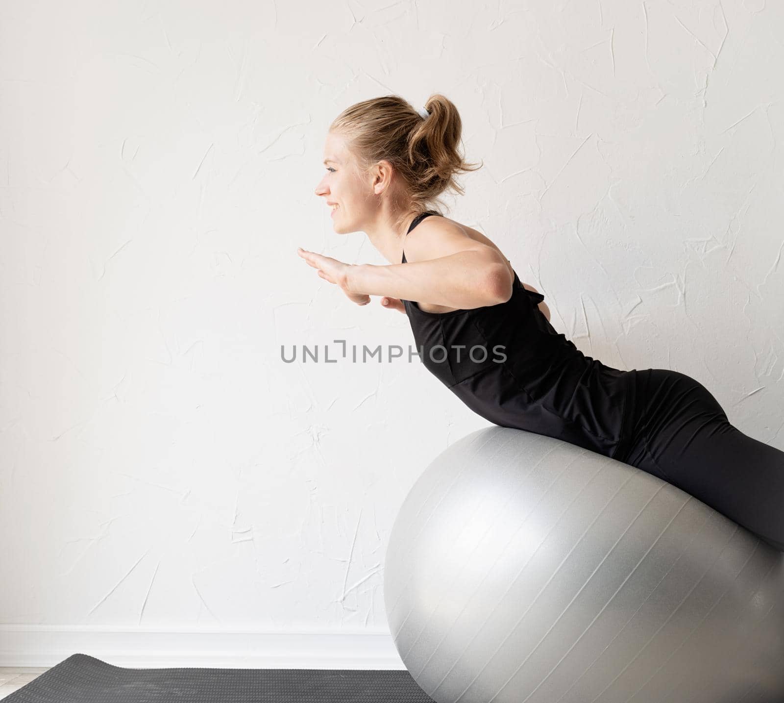 Sport and healthy lifestyle concept. Young smiling sportive woman working out on the fitness ball training her back
