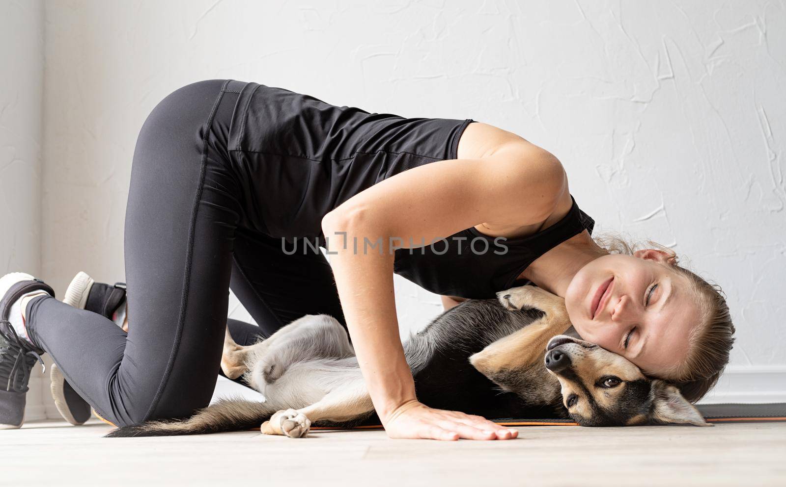 Sport and healthy lifestyle concept. Young sportive woman embracing her mixed breed dog laying on the floorat home