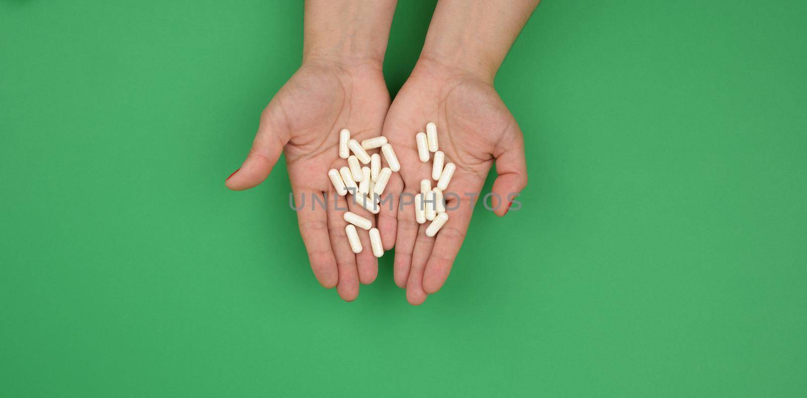 two female hands hold oval white capsules on a green background by ndanko