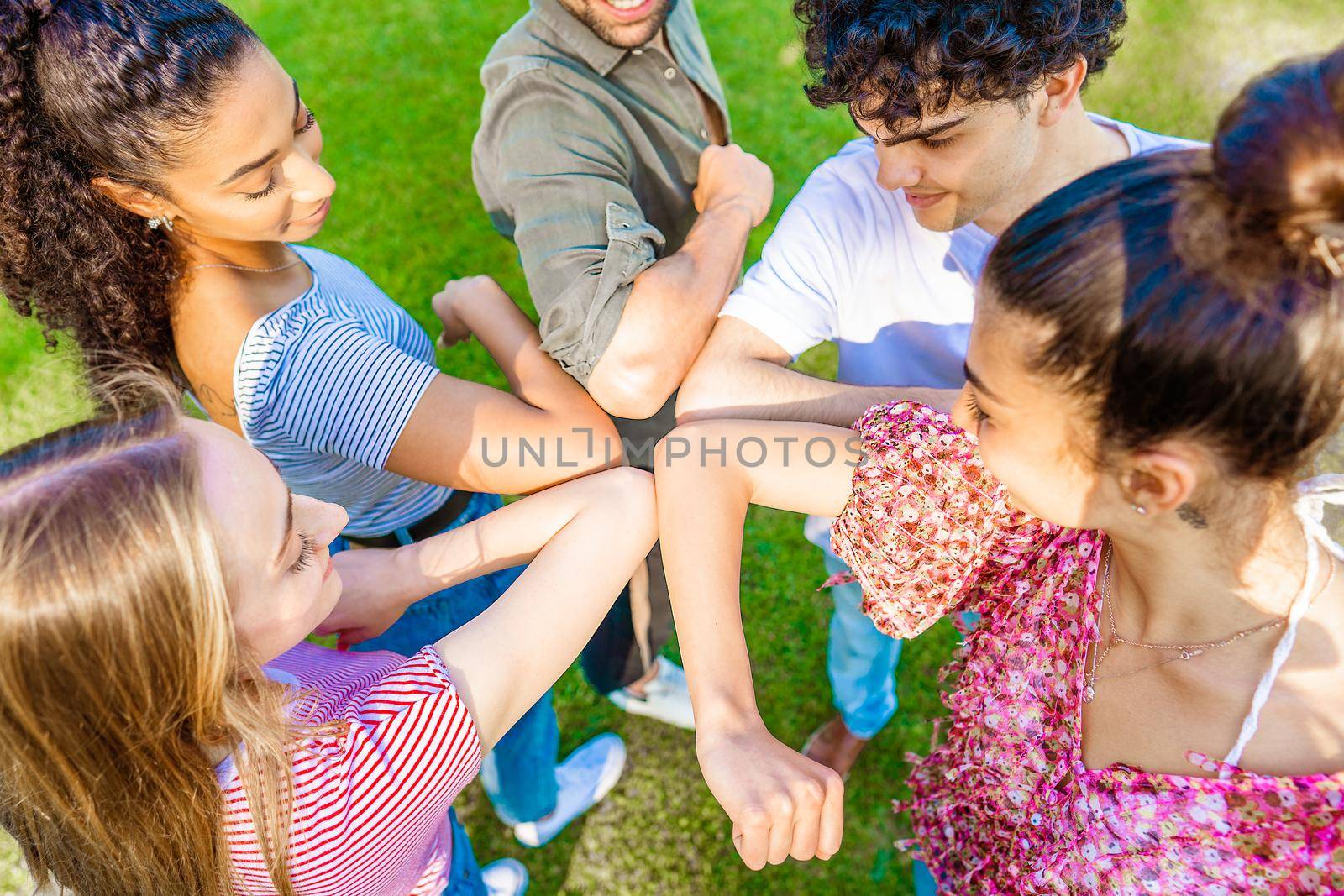 Five multiracial friends in circle bumping elbow saying hello each other for social distancing respect in pandemic time. New normal human habits for Covid-19 issue disease. Trust in future concept by robbyfontanesi
