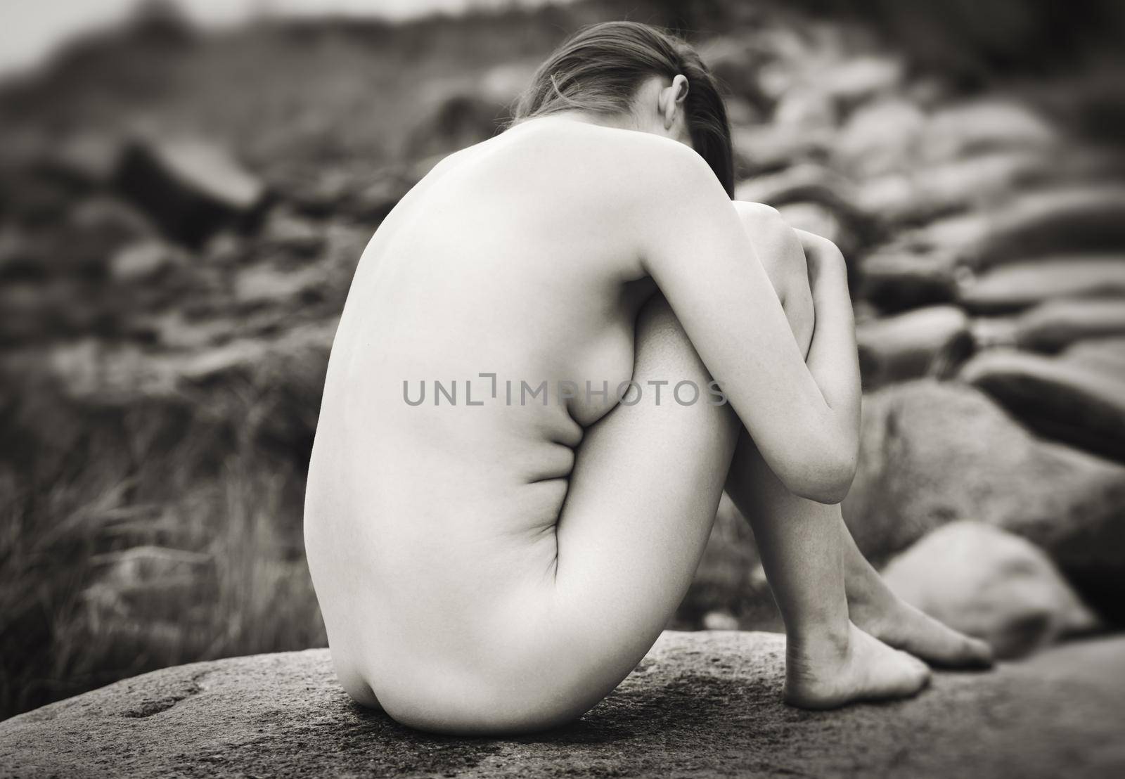 Lifestyle and beauty concept. Young nude woman enjoying nature among large stones by the sea. Naked woman on the seashore