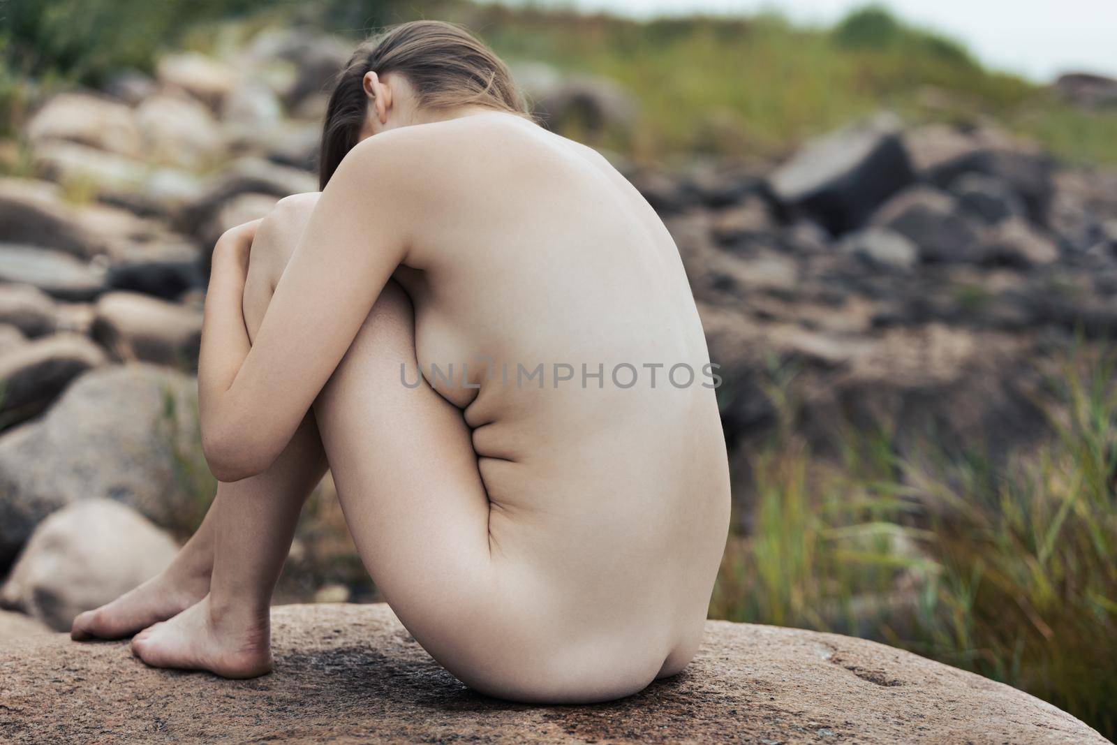 Lifestyle and beauty concept. Young nude woman enjoying nature among large stones by the sea. Naked woman on the seashore