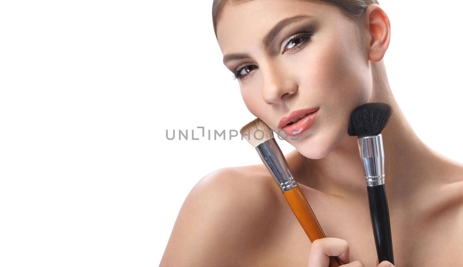 Beauty must haves. Horizontal shot of a beautiful young woman looking to the camera confidently holding makeup brushes to her face wearing professional makeup with brown smoky eyes and nude lipstick
