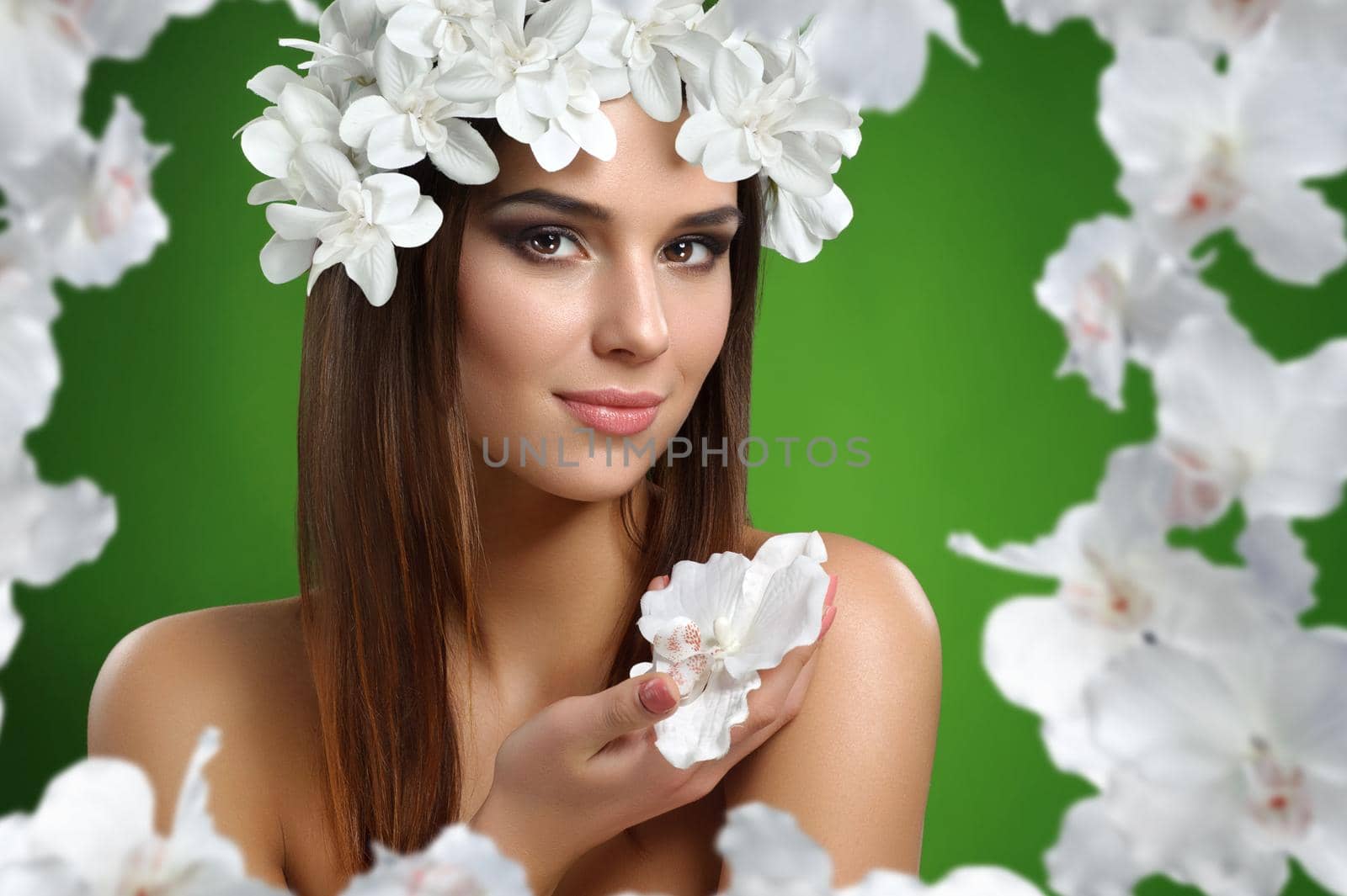 Soft tenderness. Young beautiful woman wearing flower wreath smiling warmly holding an orchid posing on green background feminine sensuality sexy beauty cosmetology skincare fashion concept