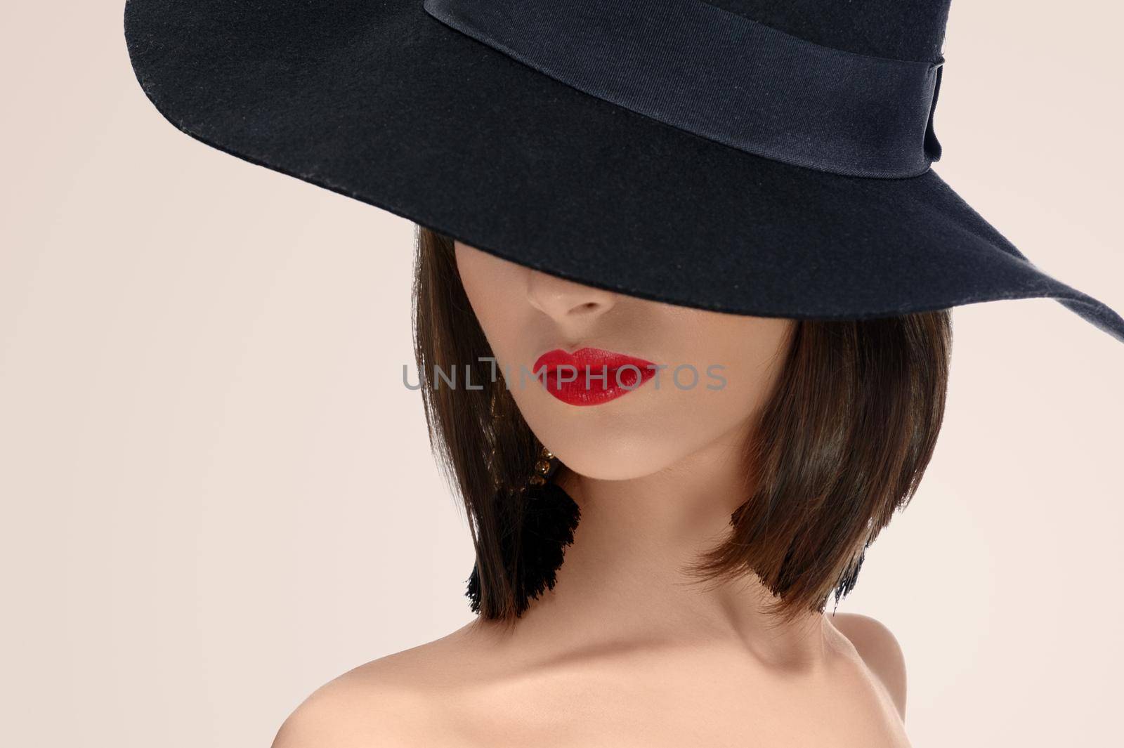 Close up studio portrait of a red lipped woman posing in a hat covering her face mystery mysterious hiding incognito anonymous red lips makeup sexy seductive secret concept .