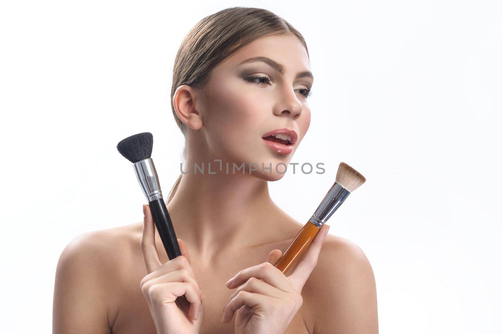Glowing beauty. Beautiful young woman with professional makeup applied posing with two makeup brushes looking away copyspace beauty cosmetics fashion style artist stylist profession industry concept