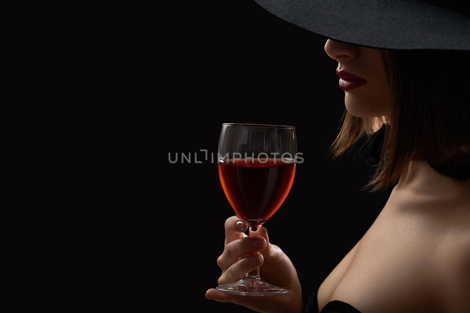 In love with wine. Cropped studio close up of a woman in a hat hiding her face holding a glass of red wine copyspace sexy hot lips seductive mysterious dark artistic shadow lighting