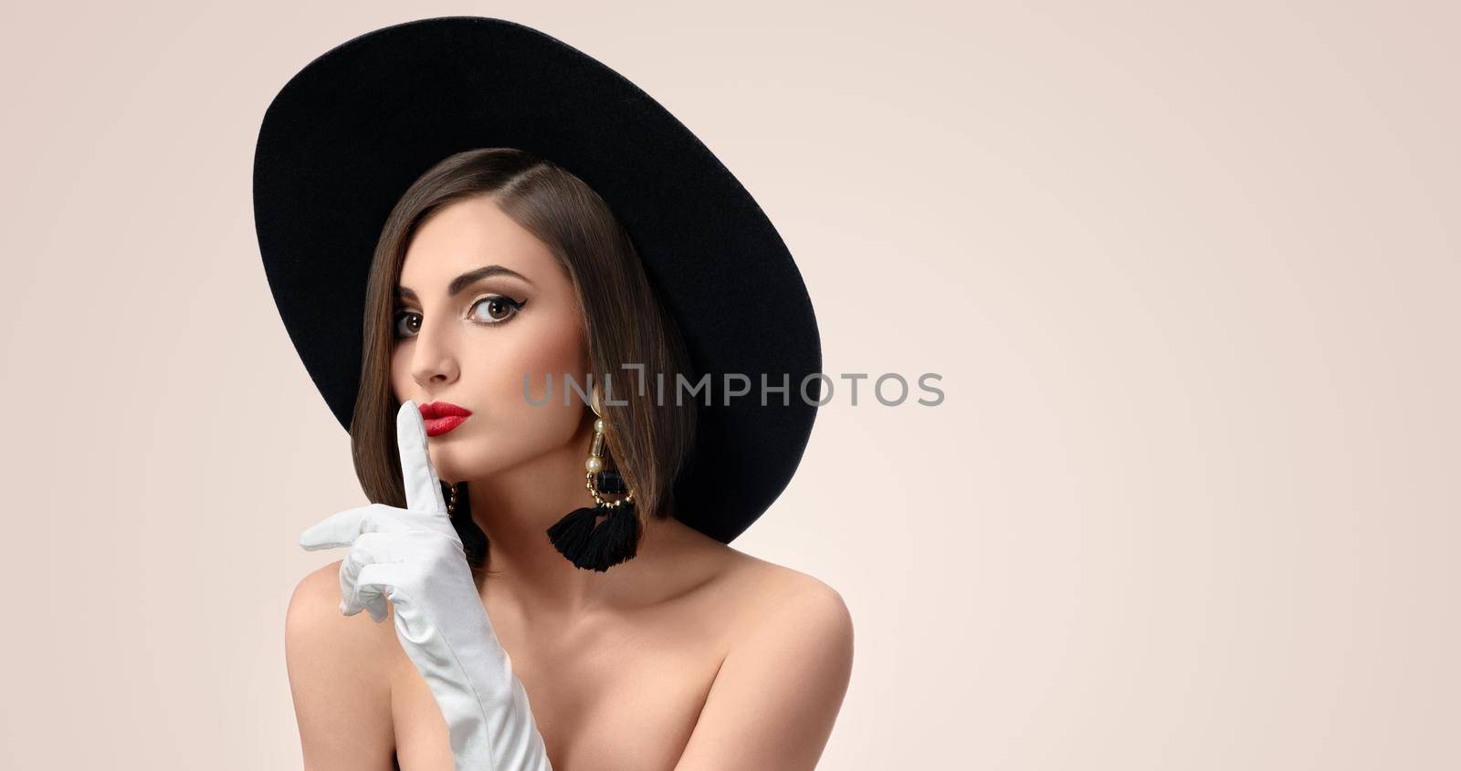 Horizontal studio portrait of a beautiful fashion model wearing a hat and gloves making shushing gesture to the camera copyspace beauty cosmetology skincare secrecy silence concept .