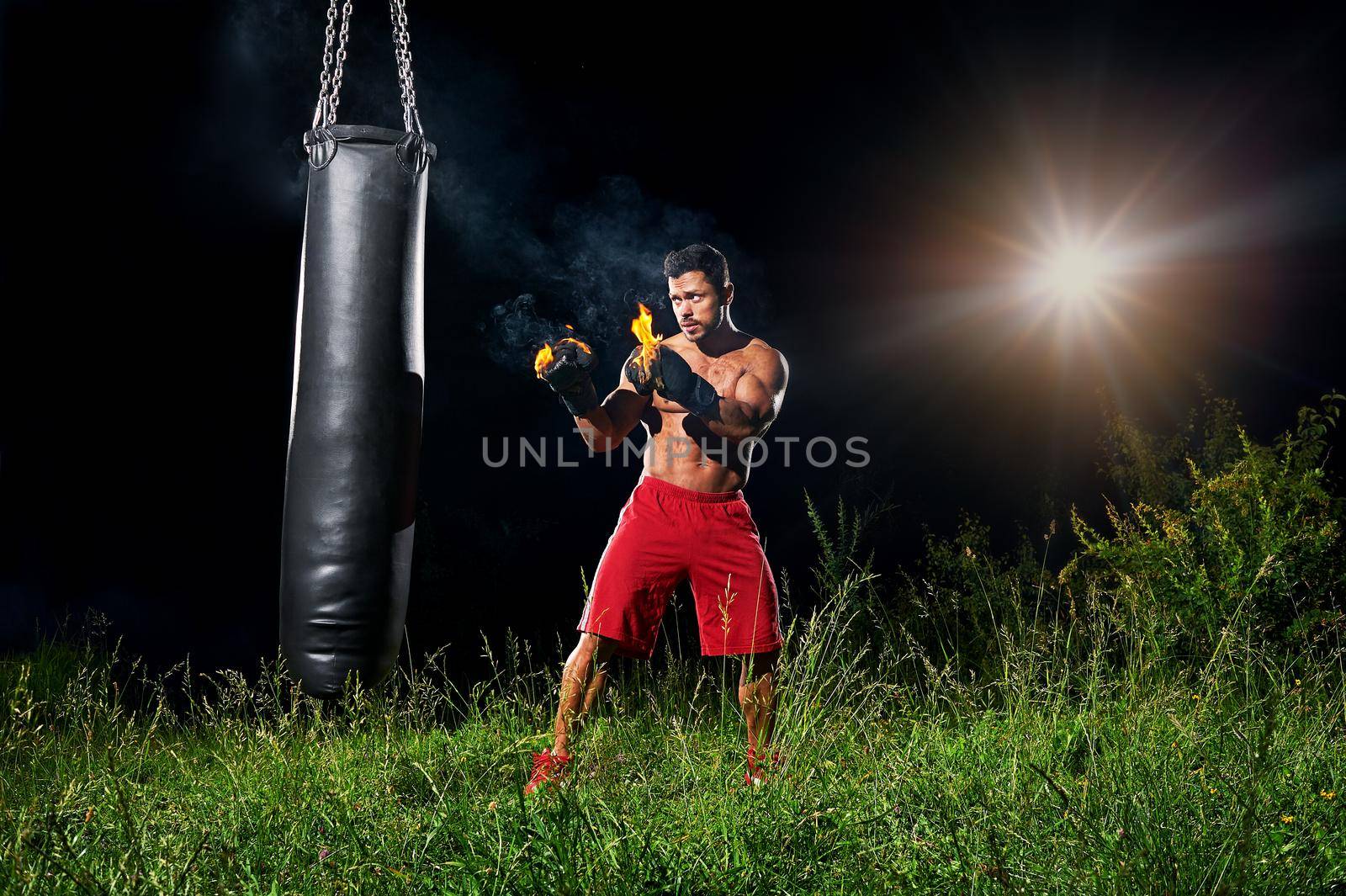 Professional boxer punching sandbag outdoors with his boxing glo by SerhiiBobyk